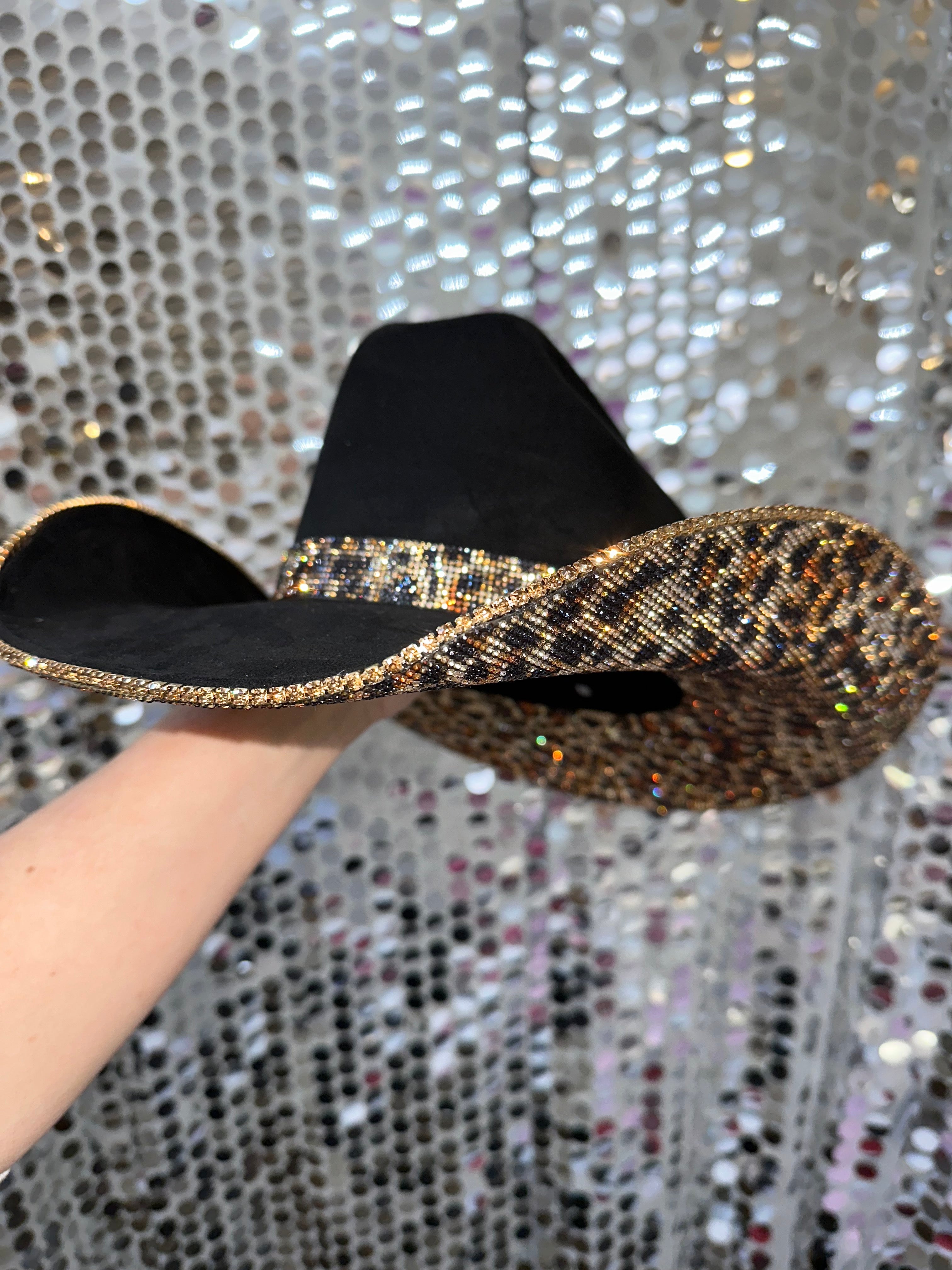 Black and gold flat sandal held by a hand against a sparkling background