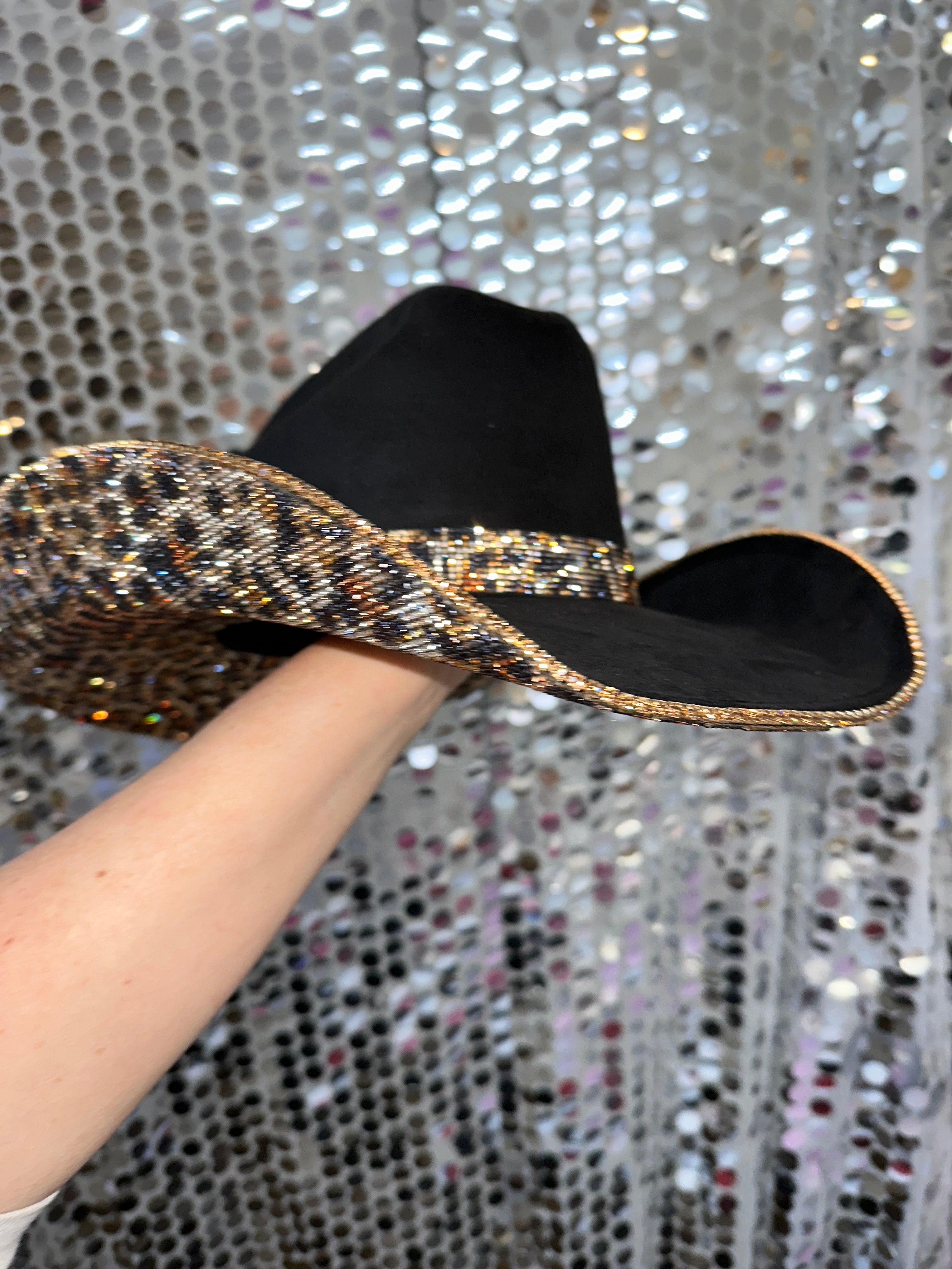 Black and gold beaded shoe held by a hand against a glittery background