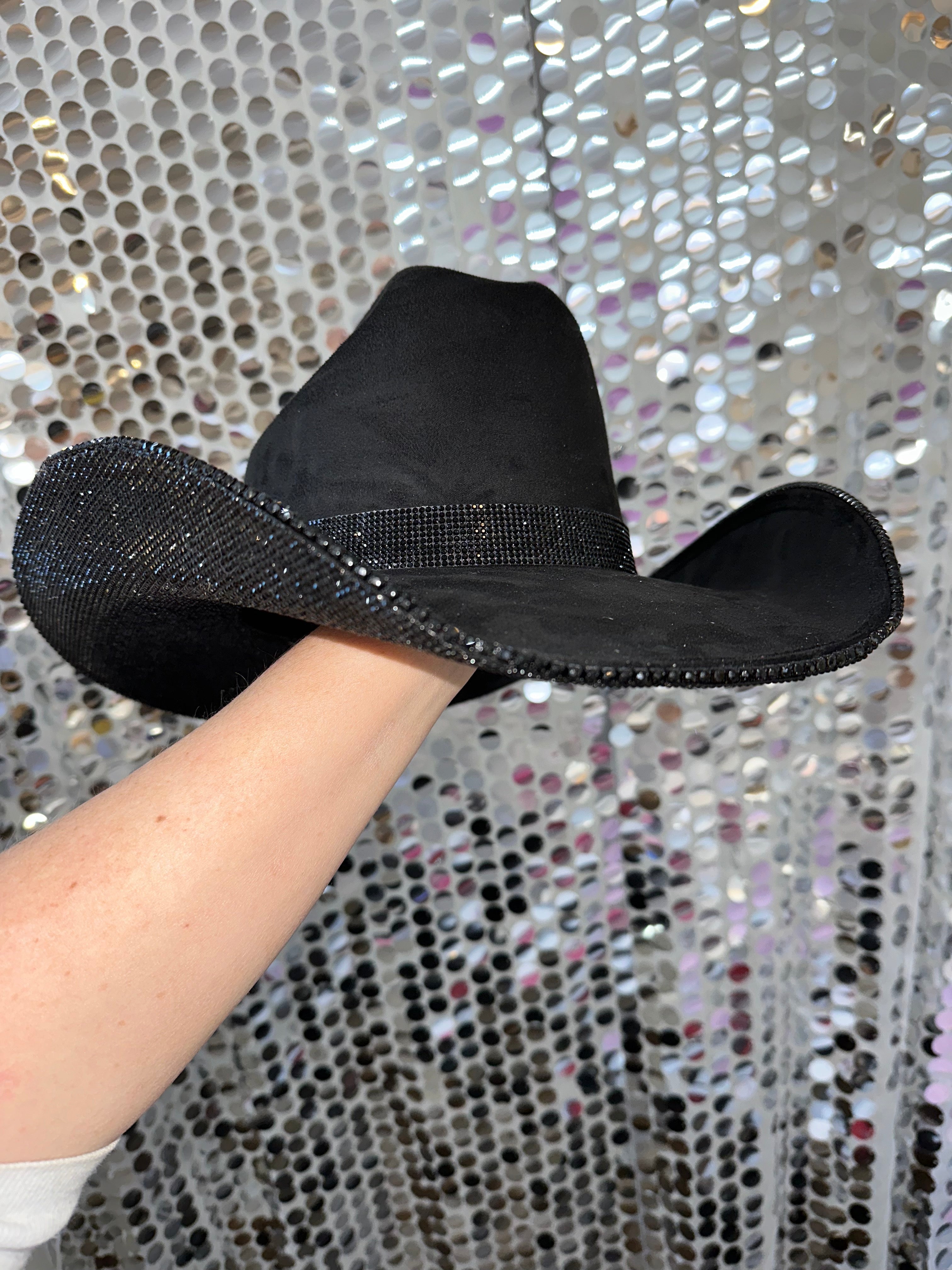 Black flat shoes with rhinestone trim worn by a person against a sequined background