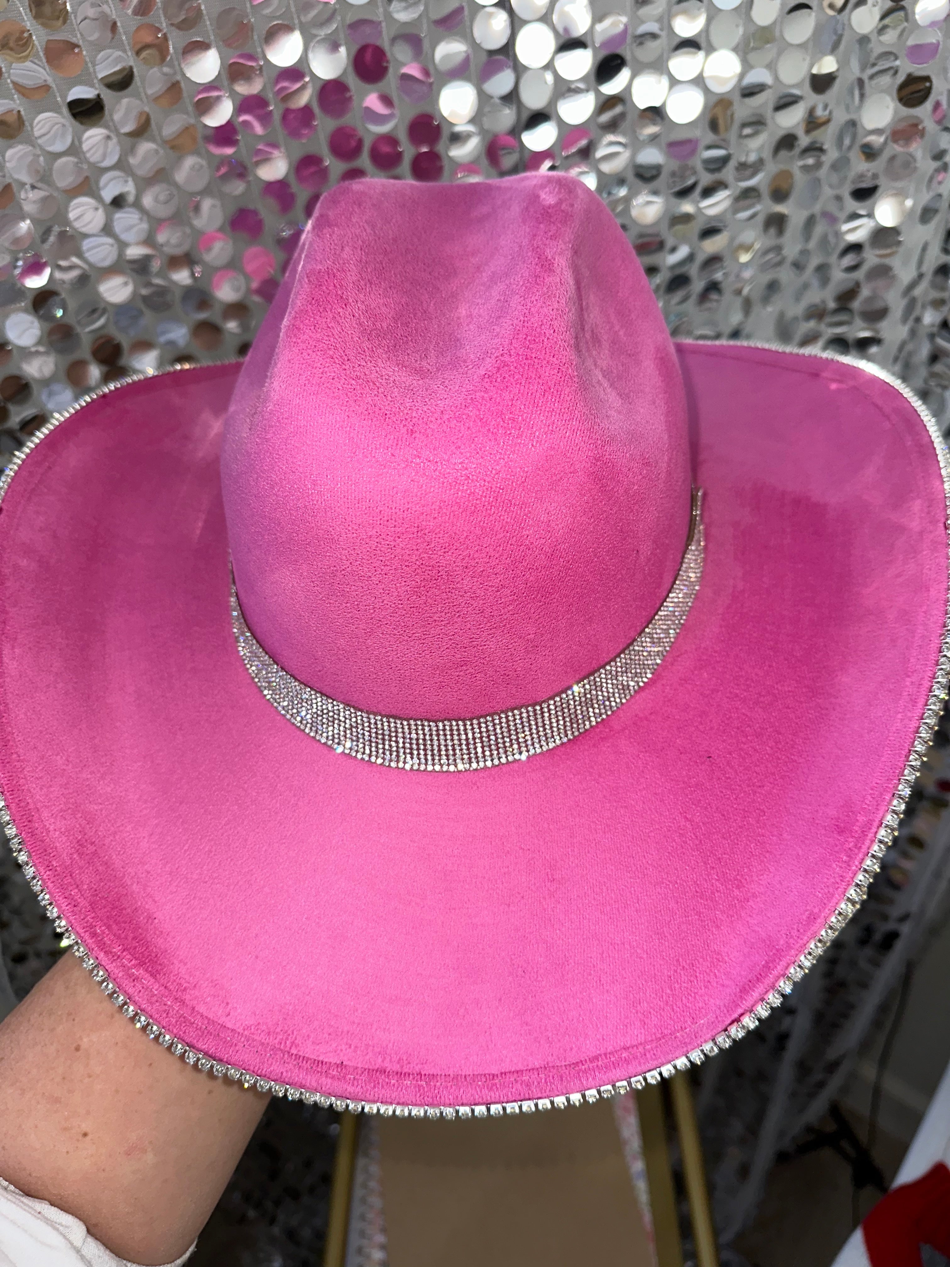 Pink cowboy hat with rhinestone band held against a reflective silver background