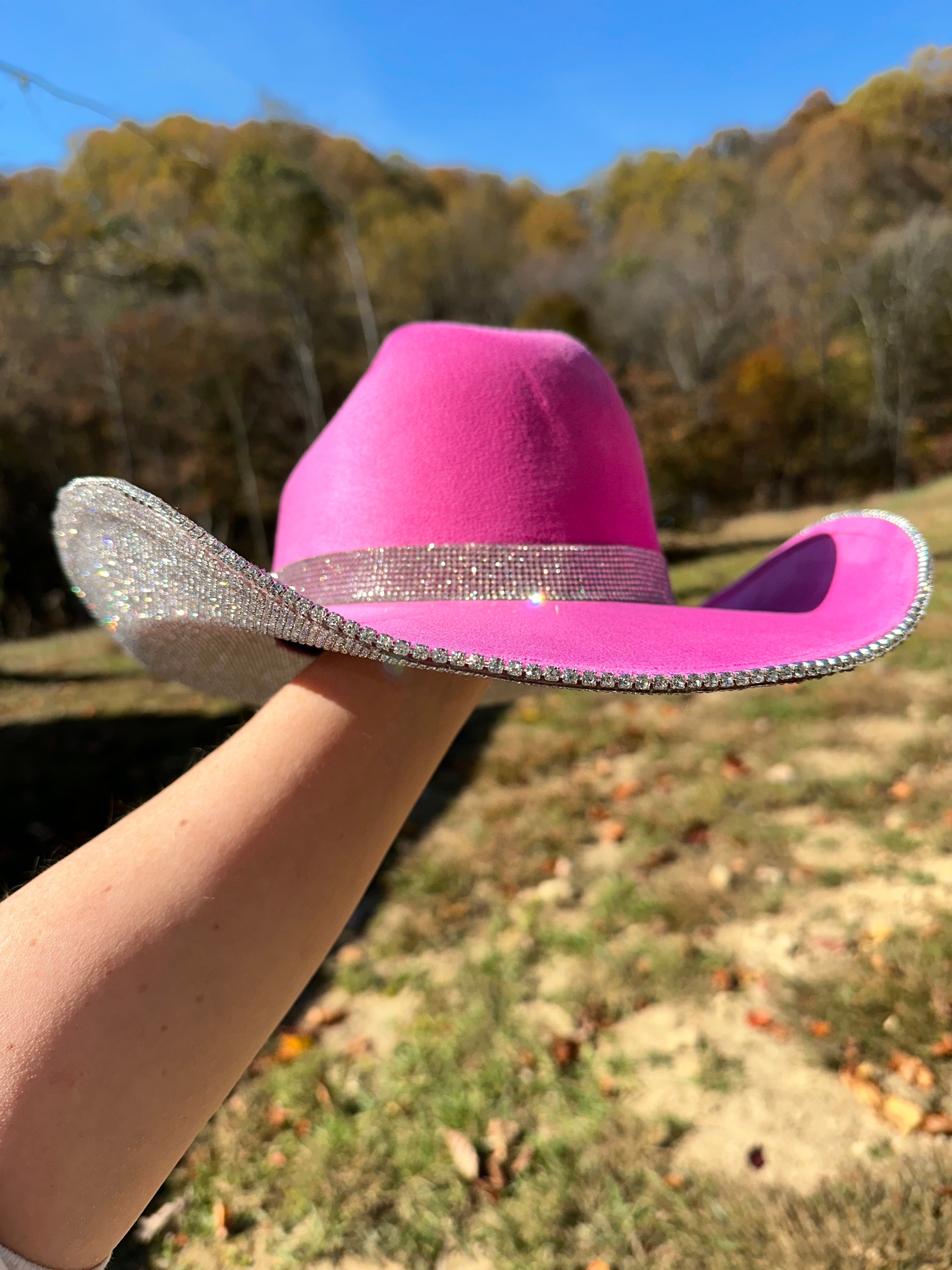 Pink cowboy hat with a glittery band held by a person outdoors.