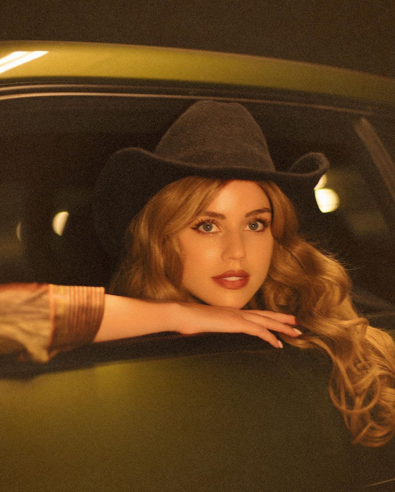 Woman wearing a black hat and brown coat sitting inside a car.