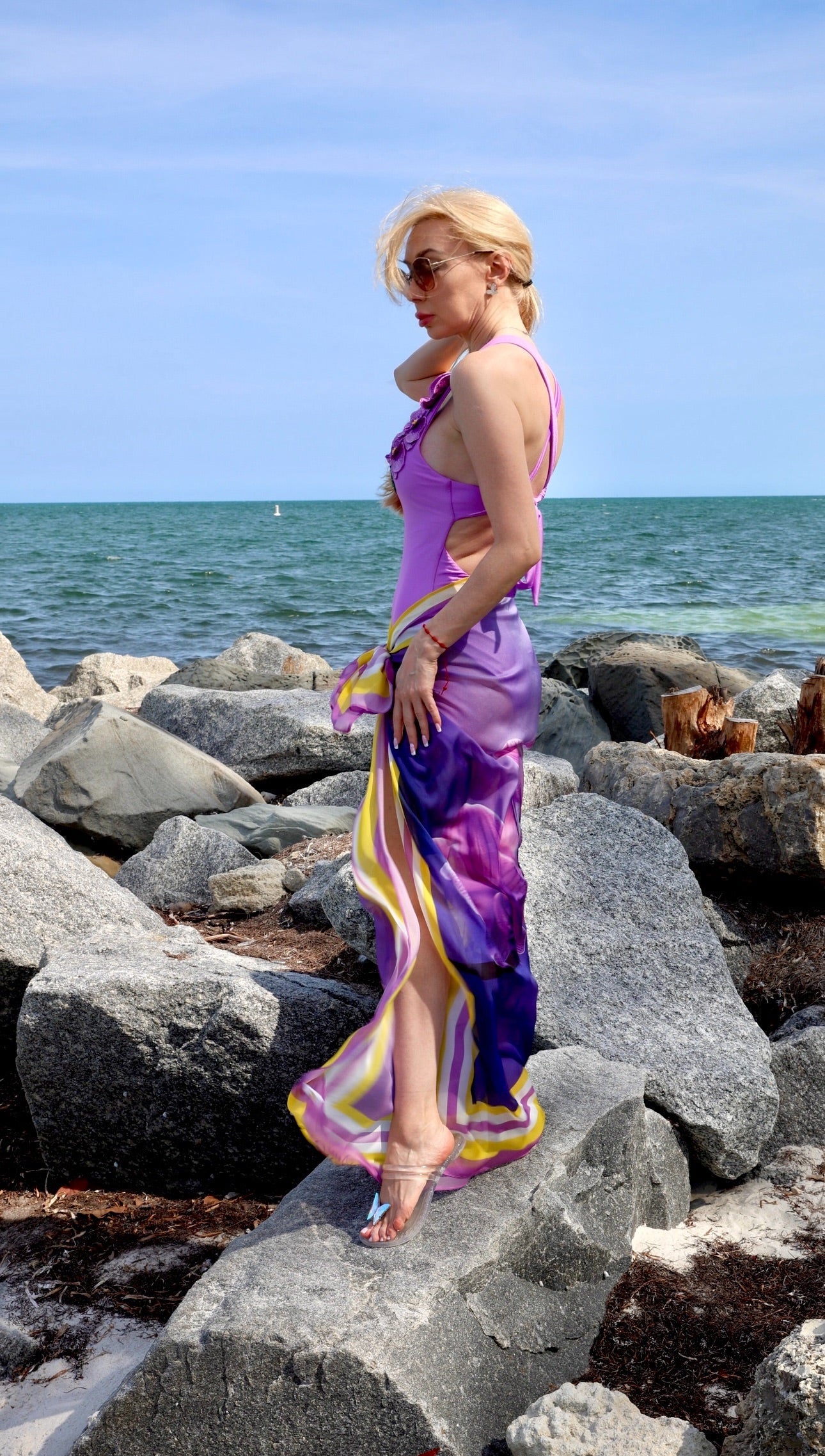 Woman in a purple dress standing on rocks by the ocean