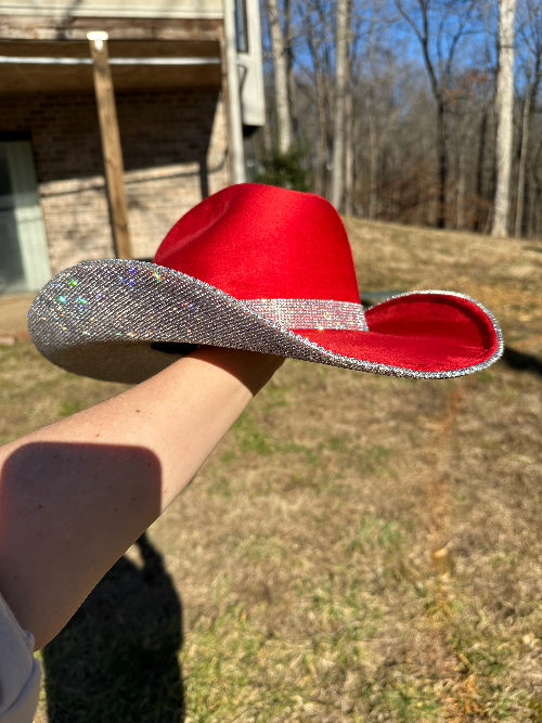 Red cowboy hat with a silver band held by a person outdoors.