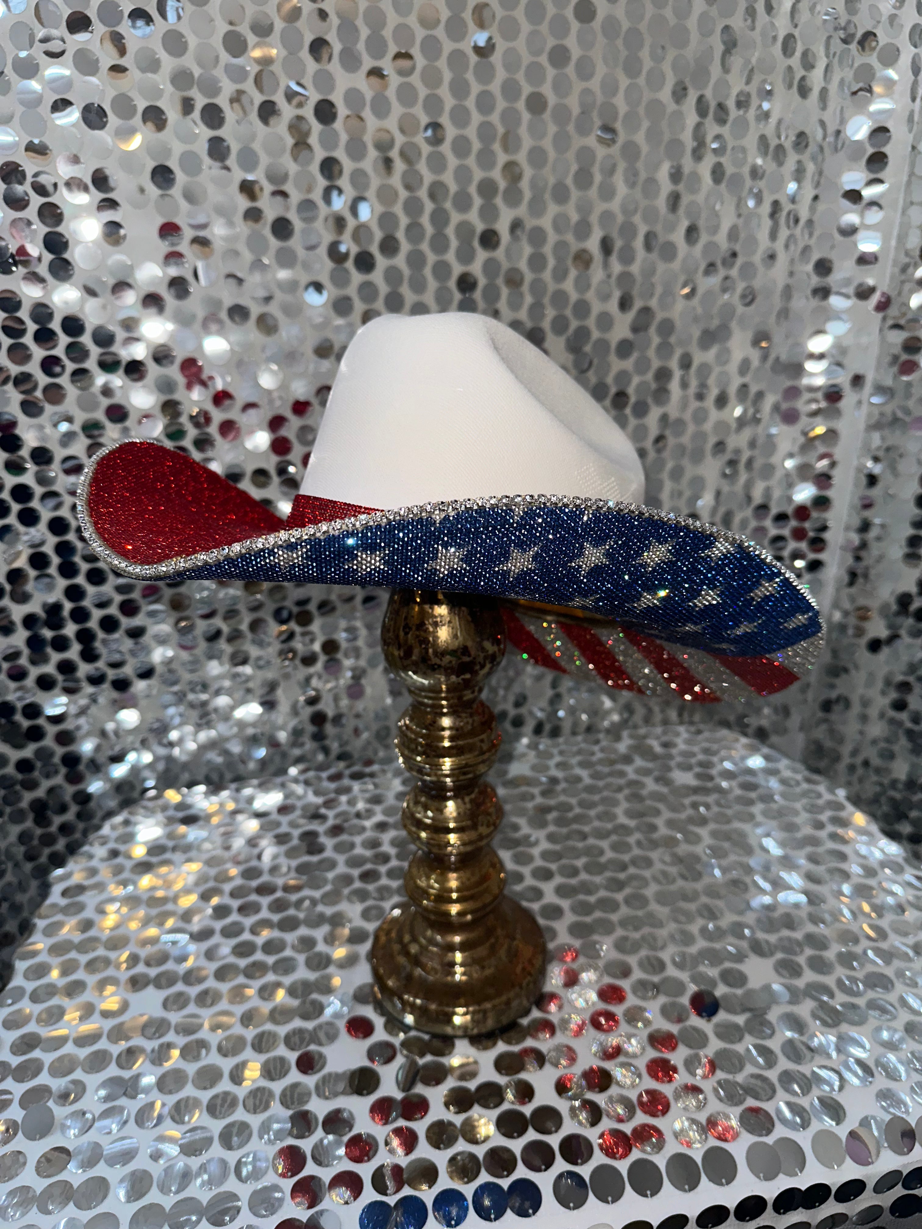 Decorative hat with American flag design on a stand against a glittery background