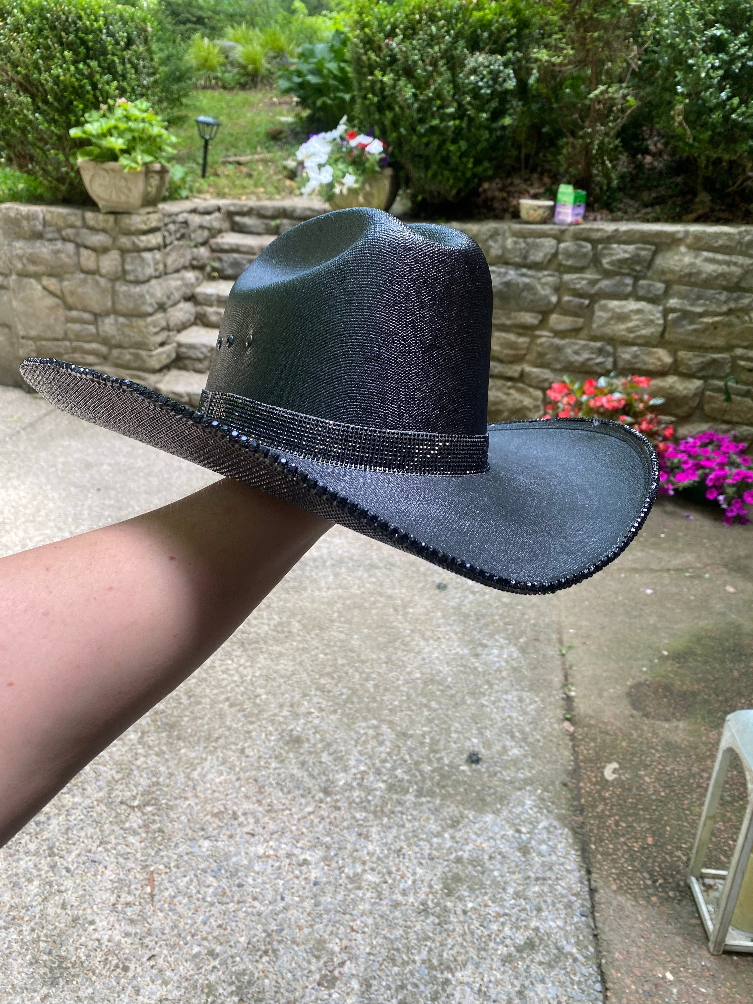 Black cowboy hat with a sequin band held by a person outdoors.