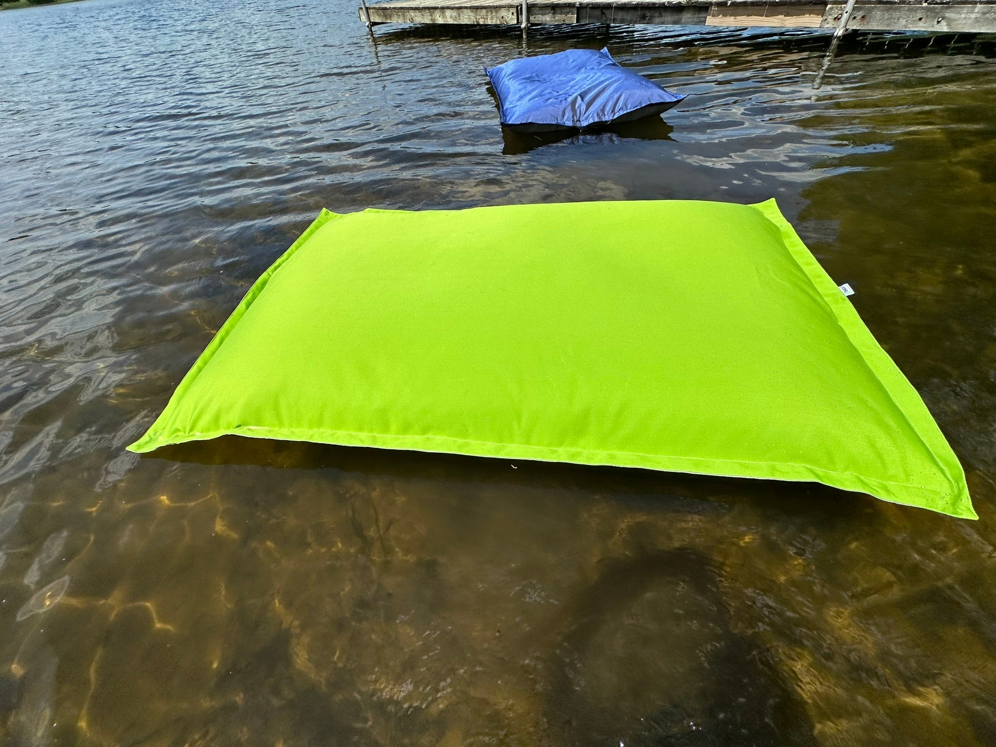 Green tarp floating on water with a dock in the background