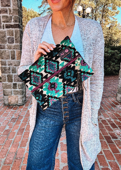 Person holding a colorful patterned pouch outdoors on a brick path.