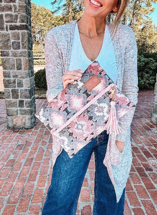 Woman holding a pink and gray patterned clutch outdoors.