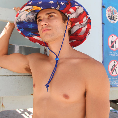 Man wearing a patriotic sun hat with an eagle design, standing against a light blue wall.
