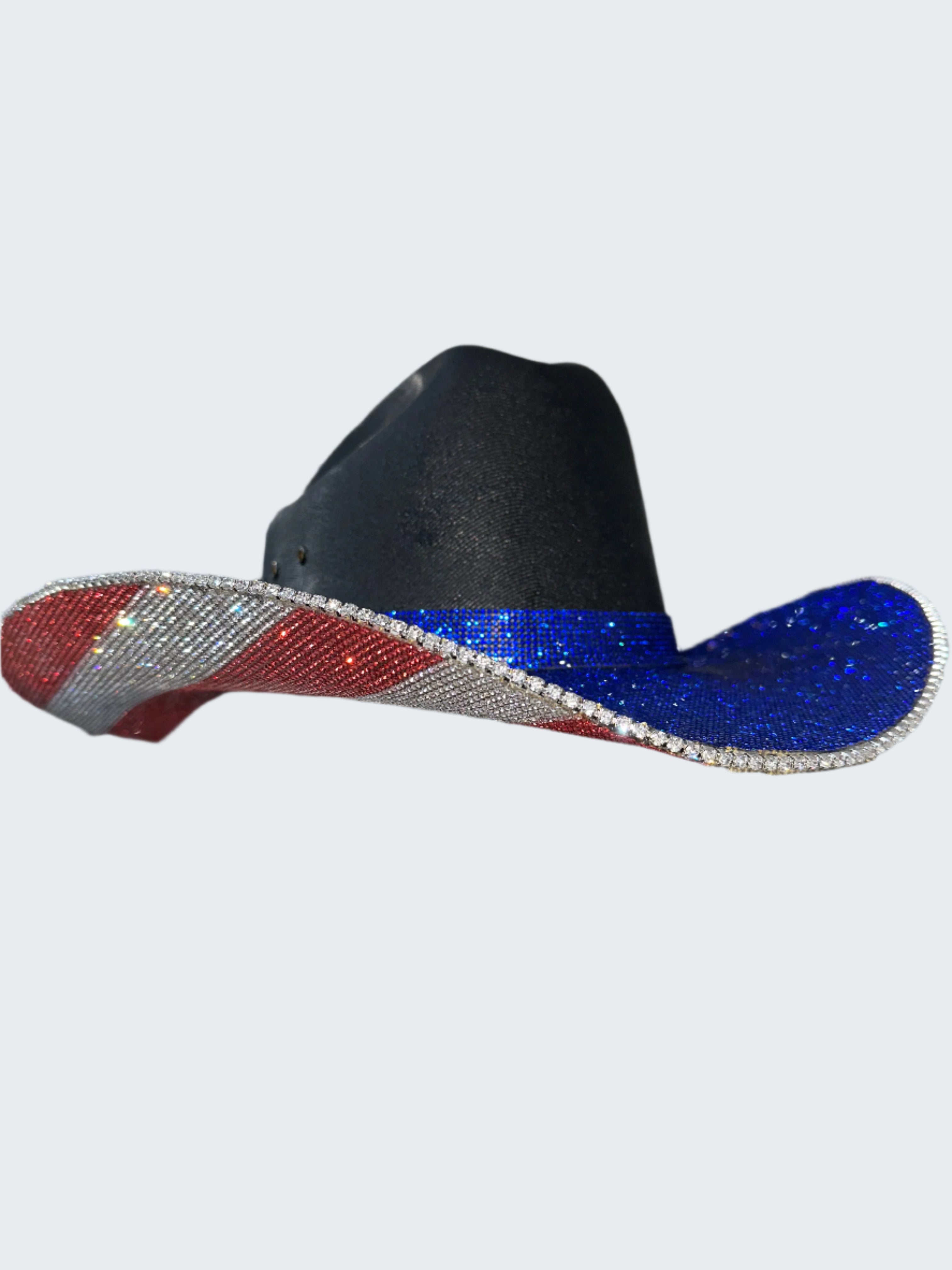 Black cowboy hat with red and blue glittery brim held by a gloved hand against a silver sequin background.