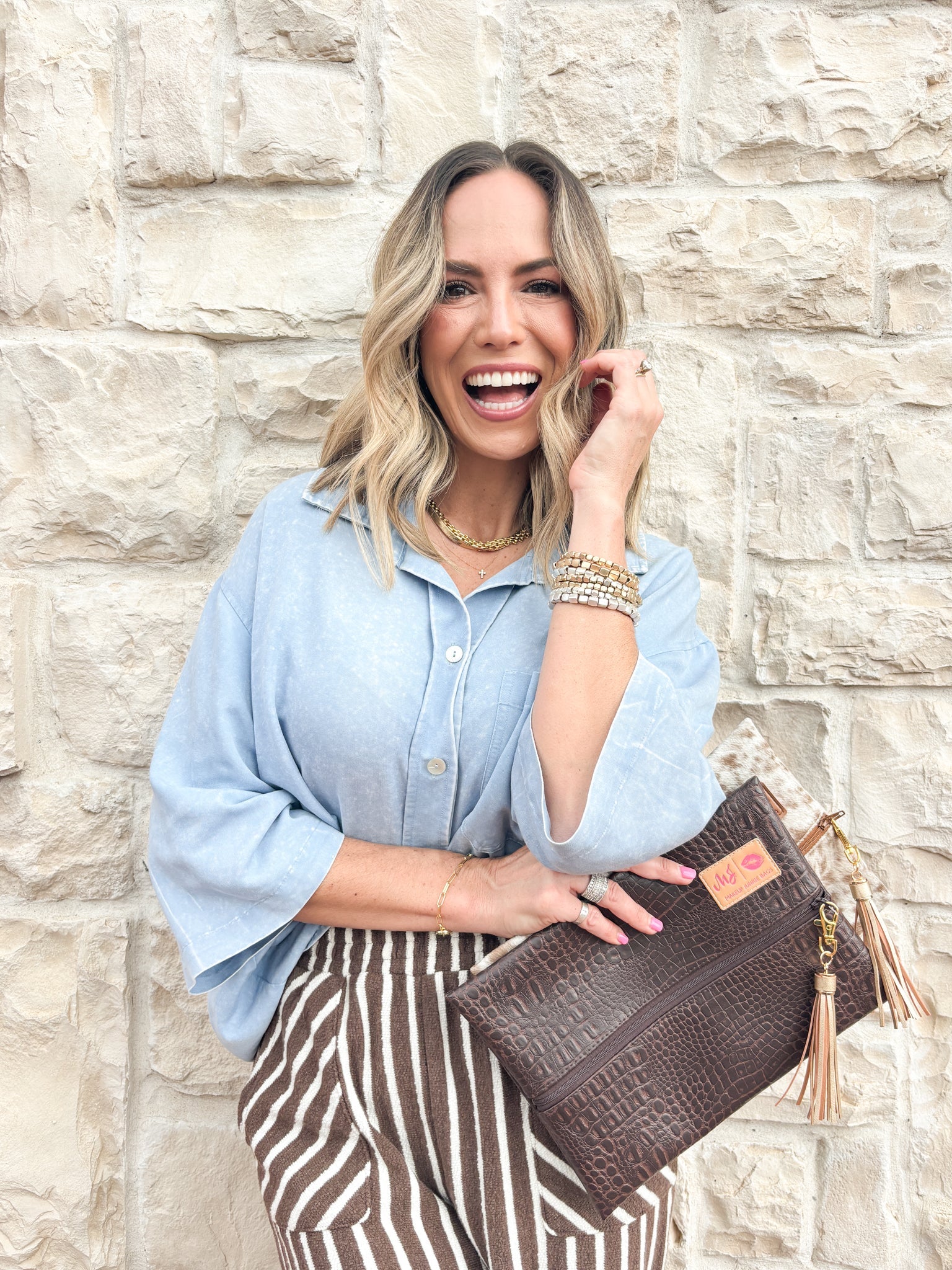 Woman holding a brown clutch against a stone wall
