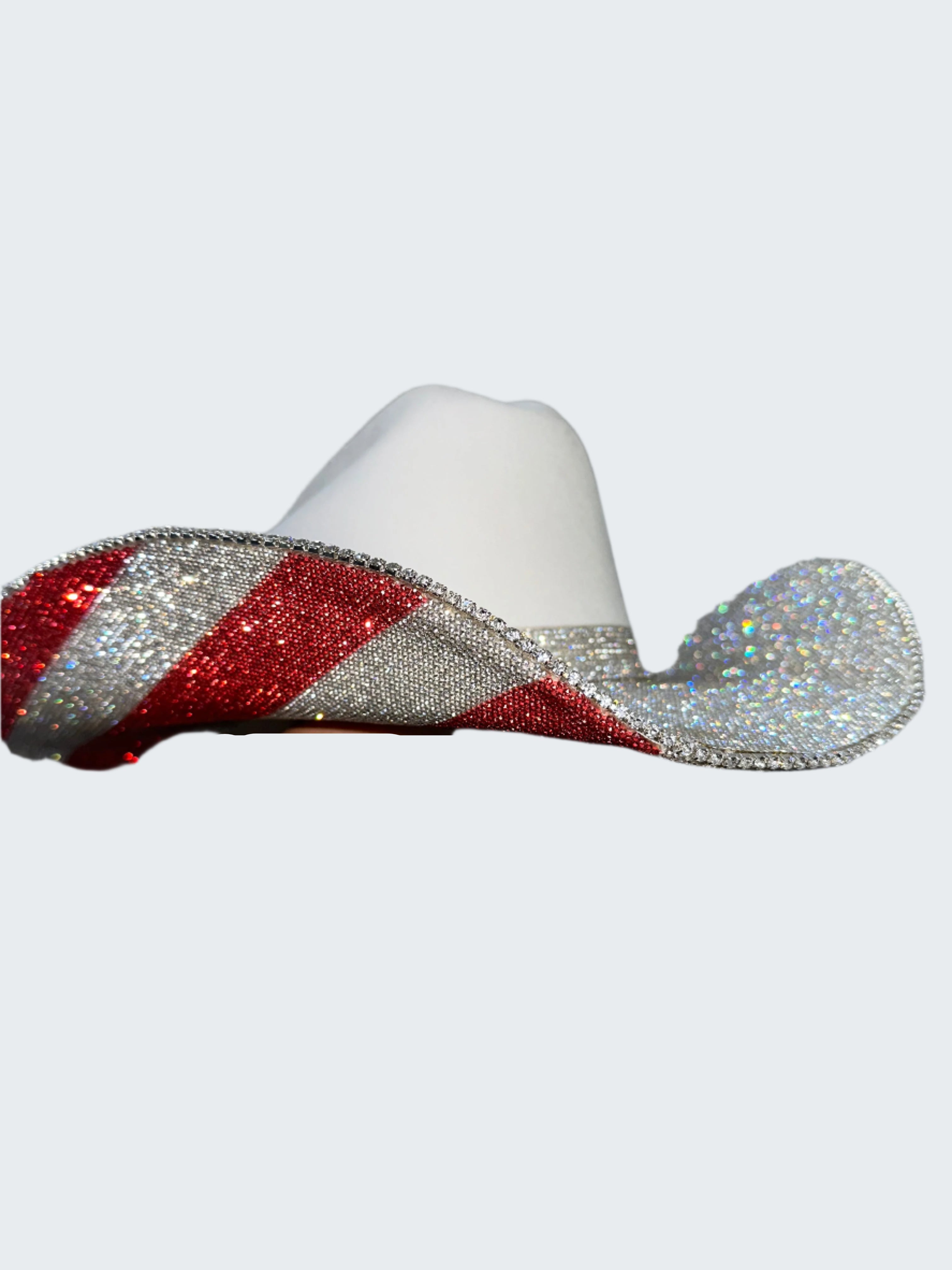 White cowboy hat with red and silver glitter band held by a hand against a glittery gray background