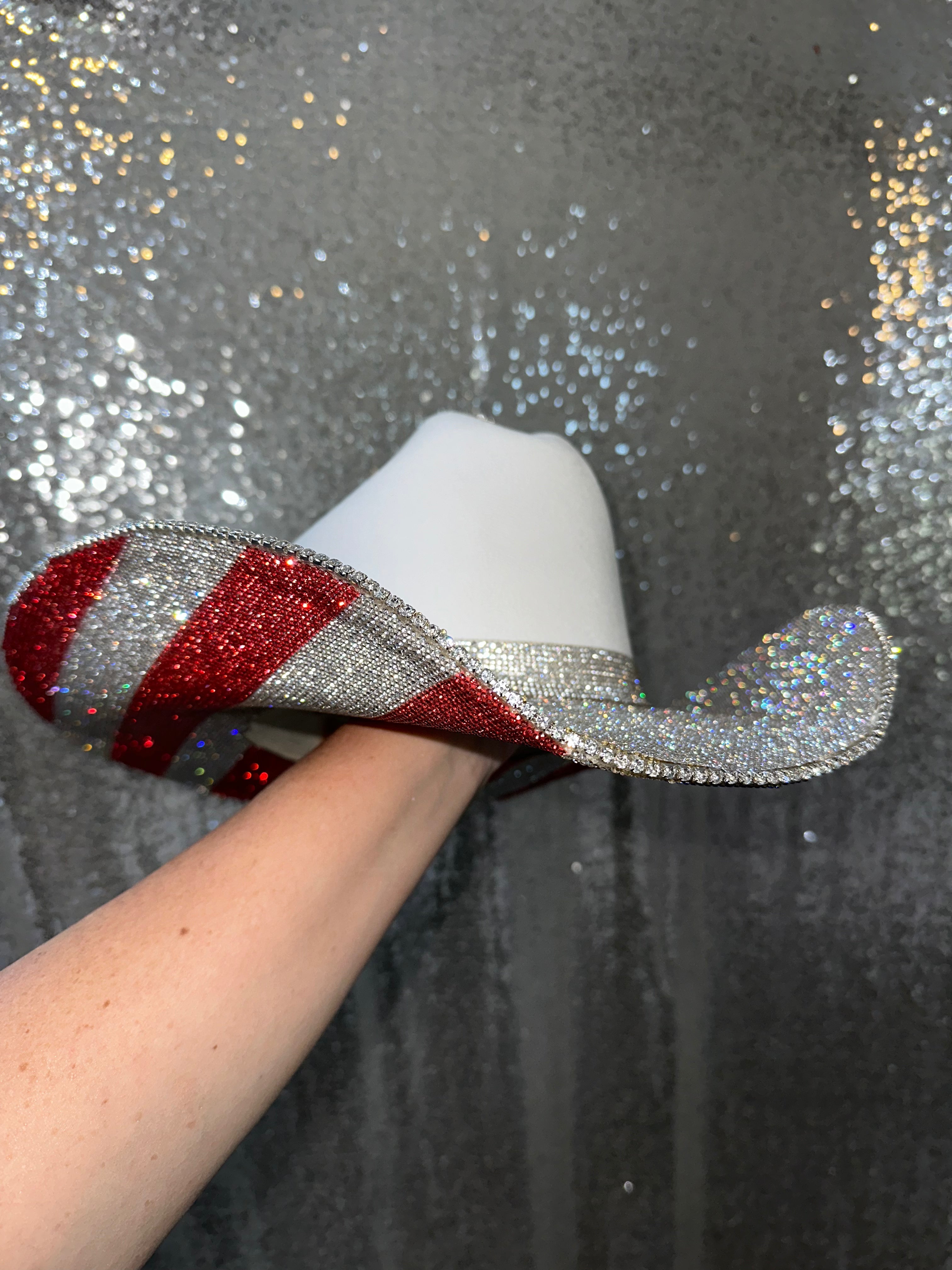 Decorative candy cane with red and silver glittery stripes held by a hand against a sparkly background.