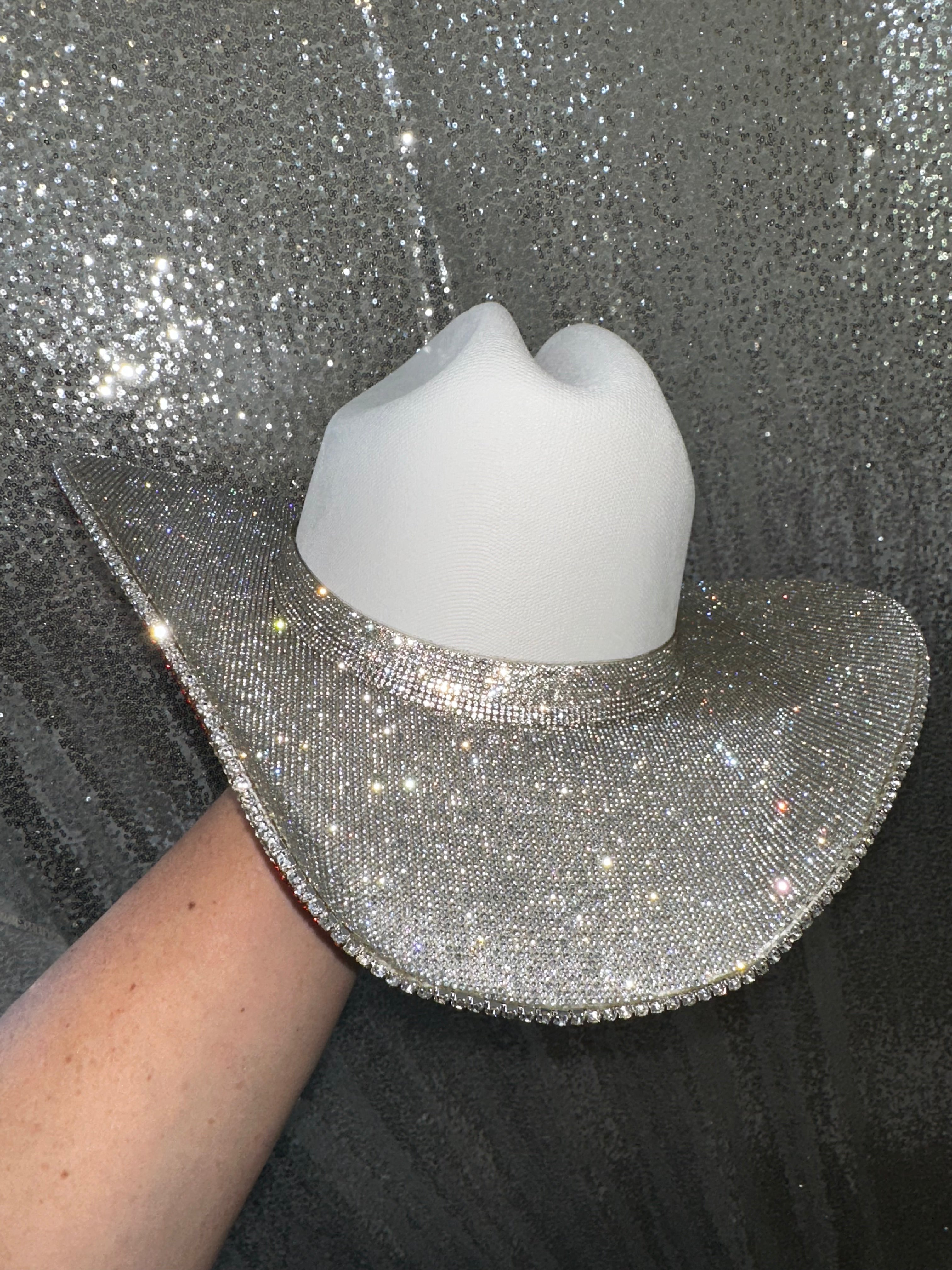 White cowboy hat with a silver glittery brim against a glittery black background