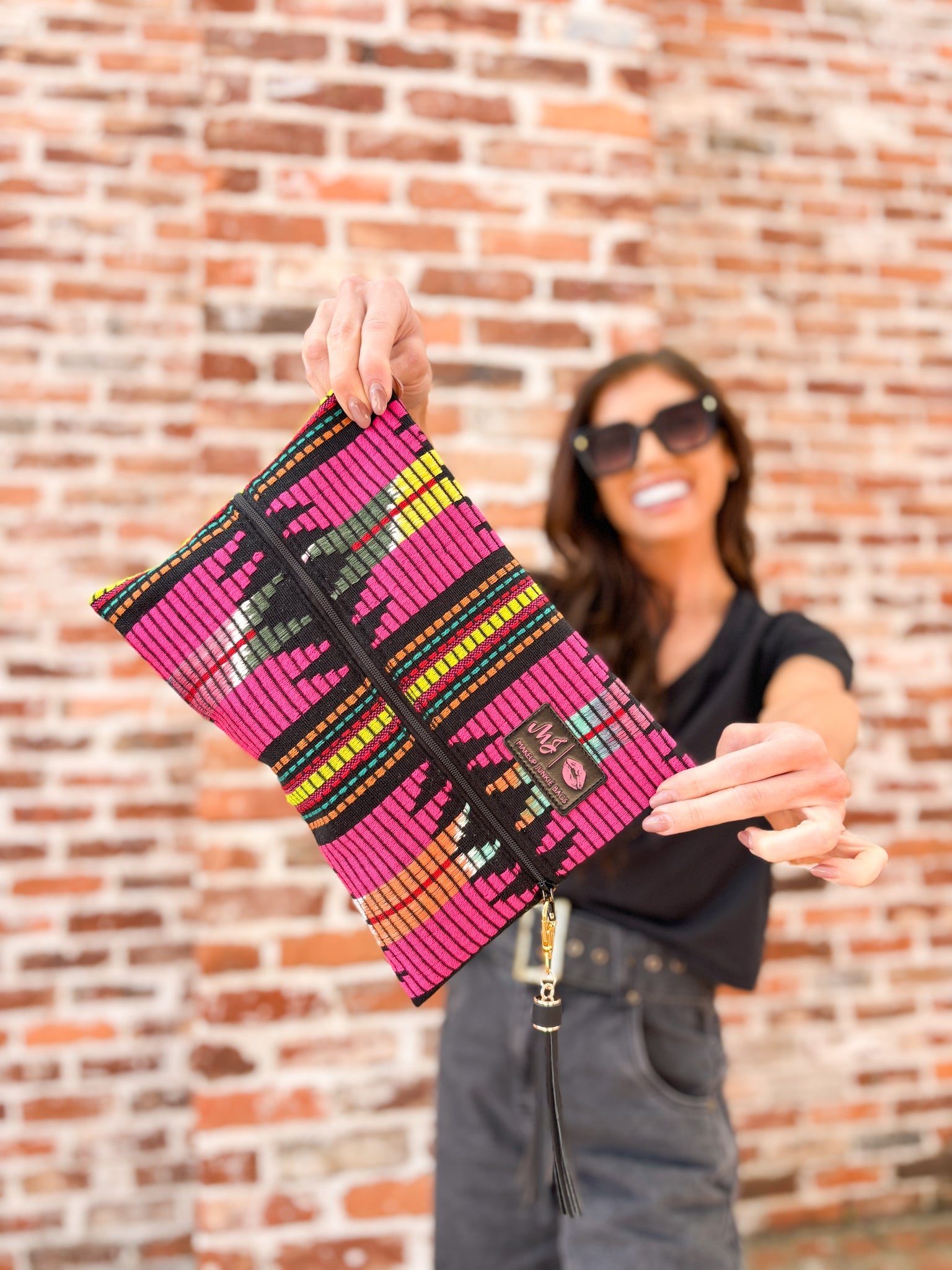 Person holding a colorful patterned clutch against a brick wall