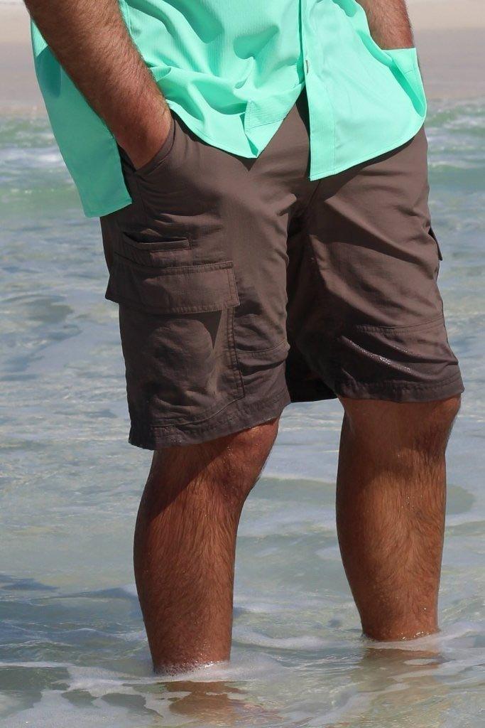 Person wearing a light green shirt and brown shorts standing in shallow water.