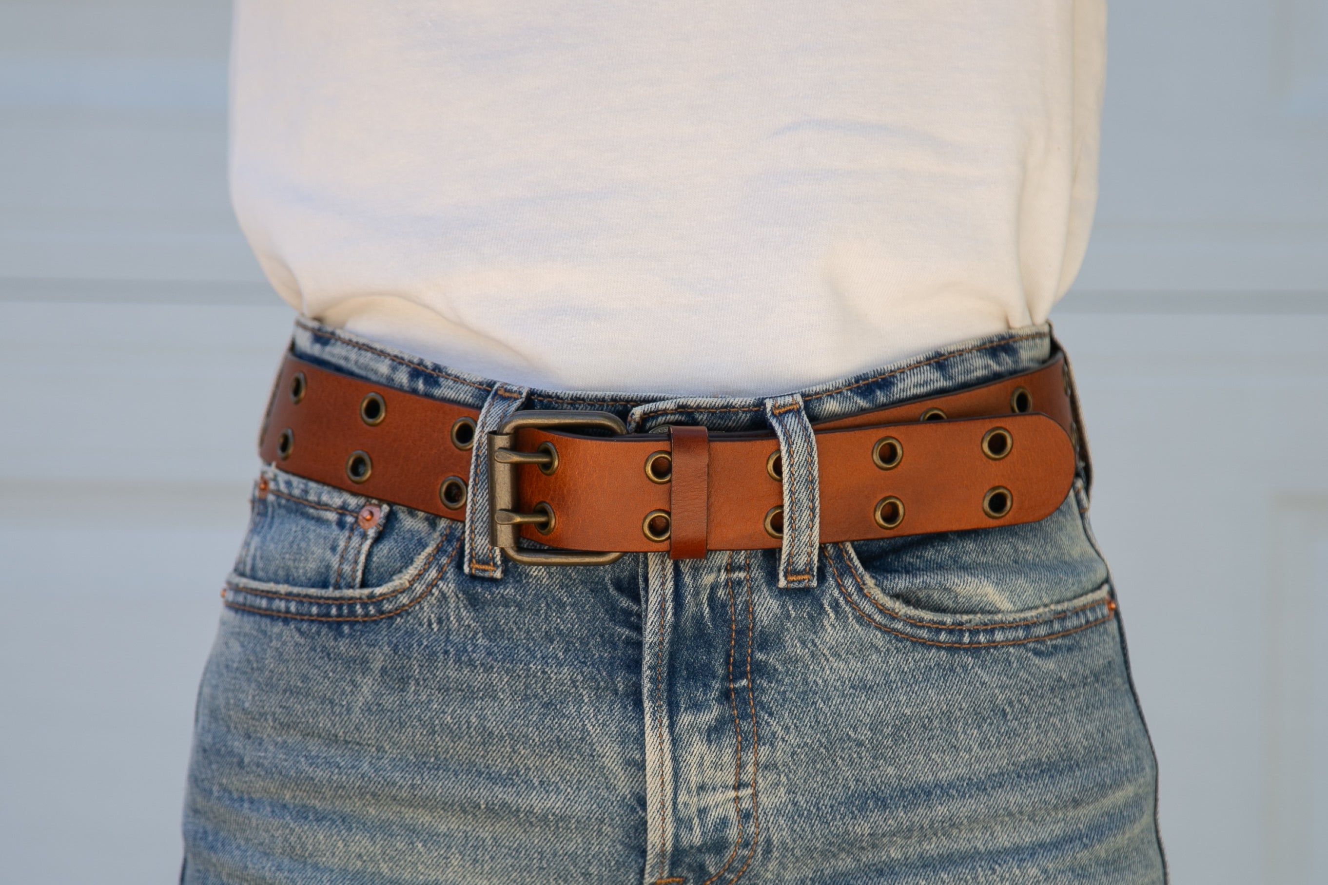 Person wearing blue jeans with a brown leather belt against a light background