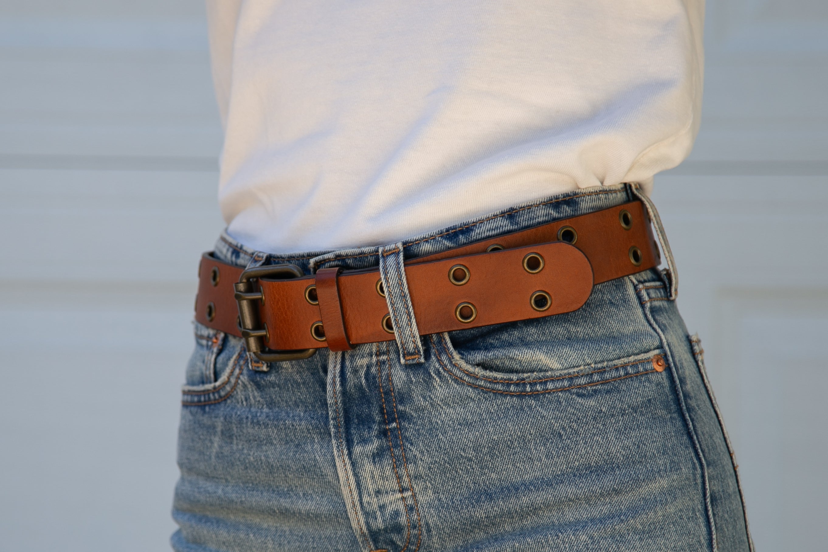 Person wearing a white shirt, blue jeans, and a brown leather belt with gold buckle.