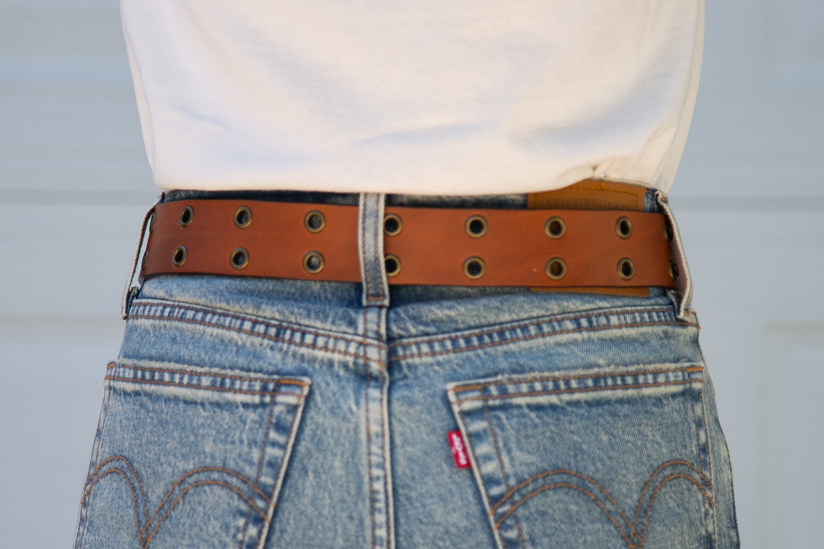 Close-up of a person wearing blue jeans with a brown belt and Levi's logo.