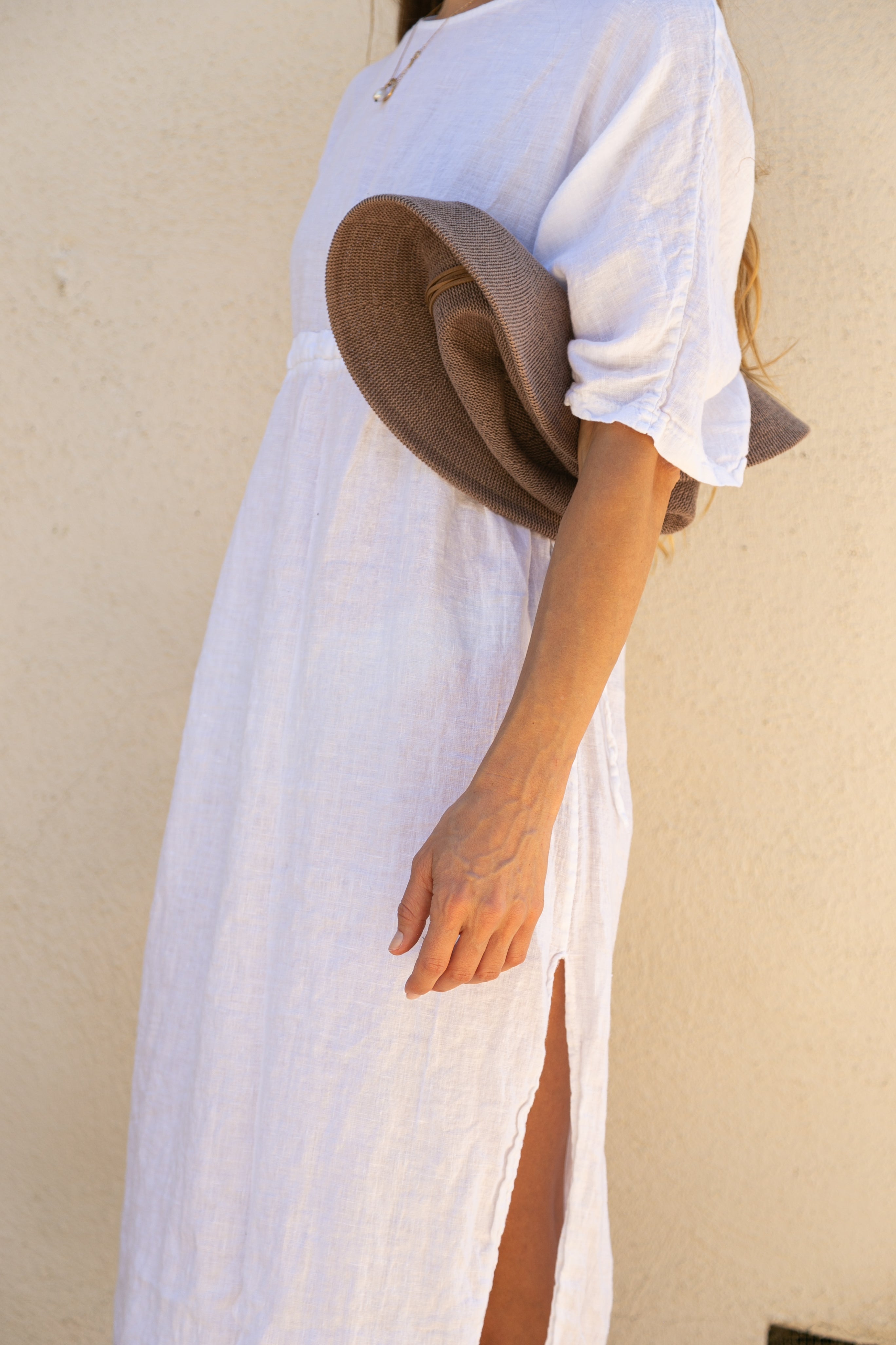 Person wearing a white dress with a brown hat against a beige wall