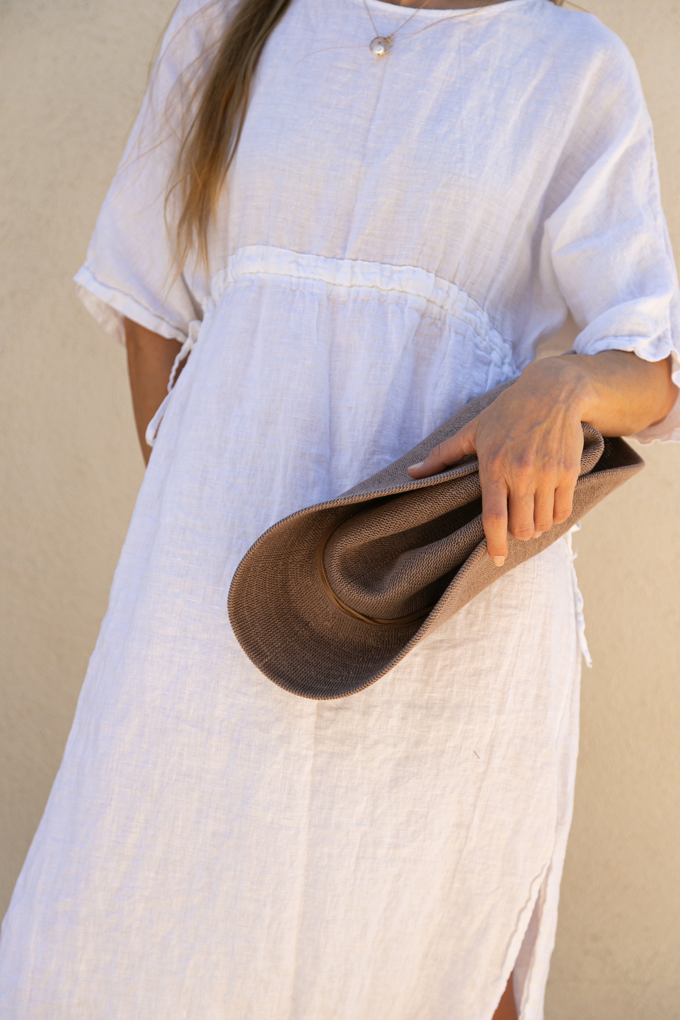Person wearing a white dress holding a brown bag against a beige background