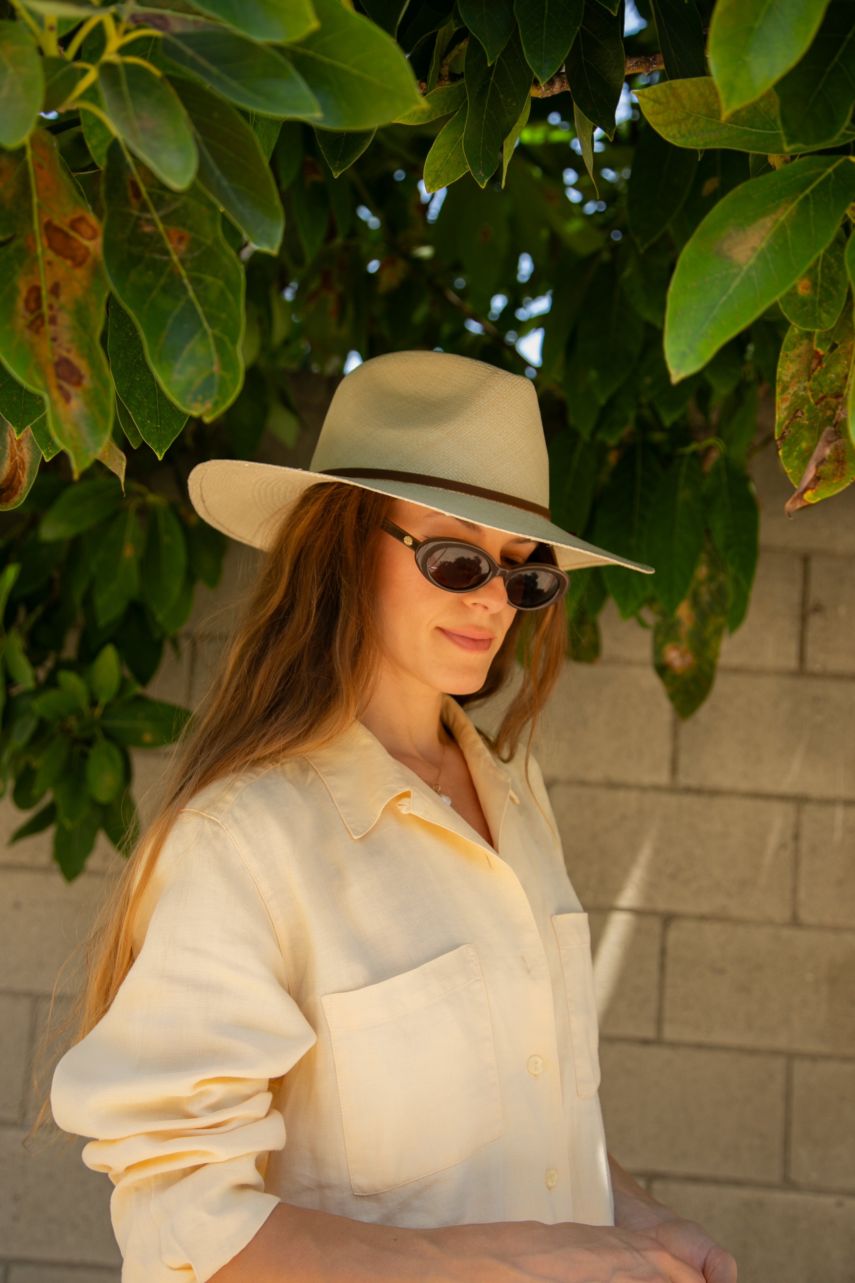 Woman wearing a beige hat and sunglasses against a leafy background