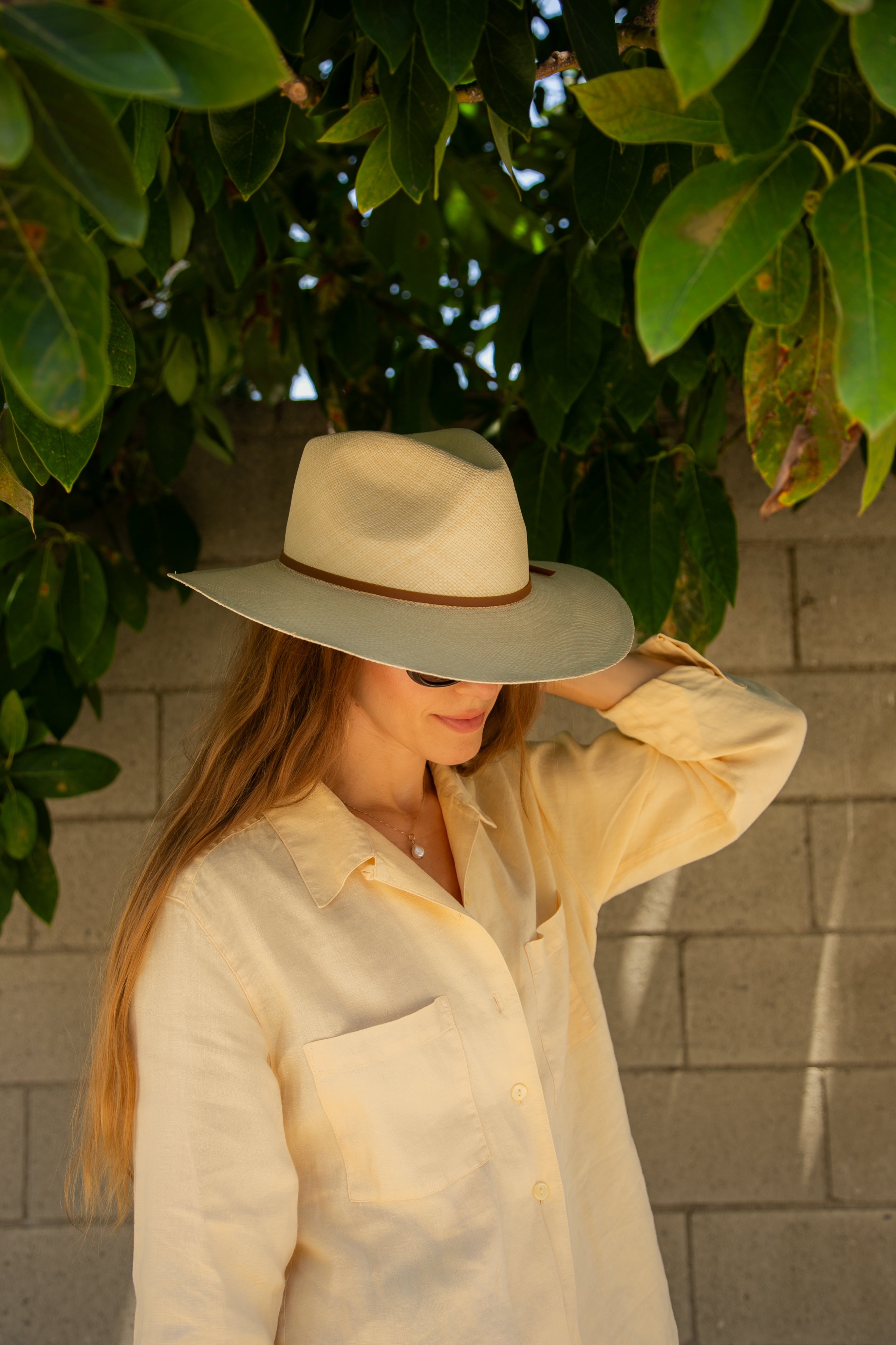 Woman wearing a wide-brimmed hat in front of a leafy background