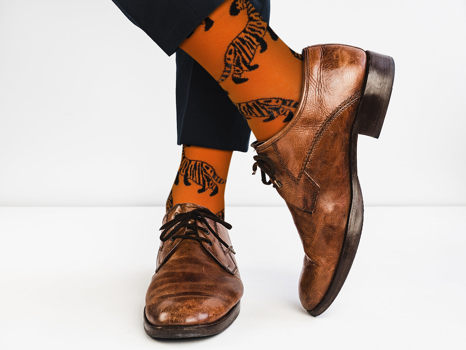 Brown leather shoes and black pants with orange socks featuring black designs on a white background
