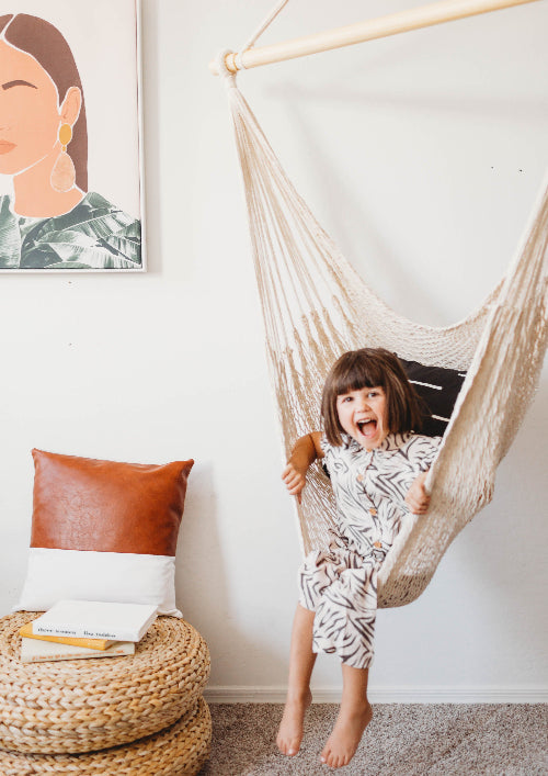 Child in a hanging chair in a room with a pillow and framed picture on the wall.