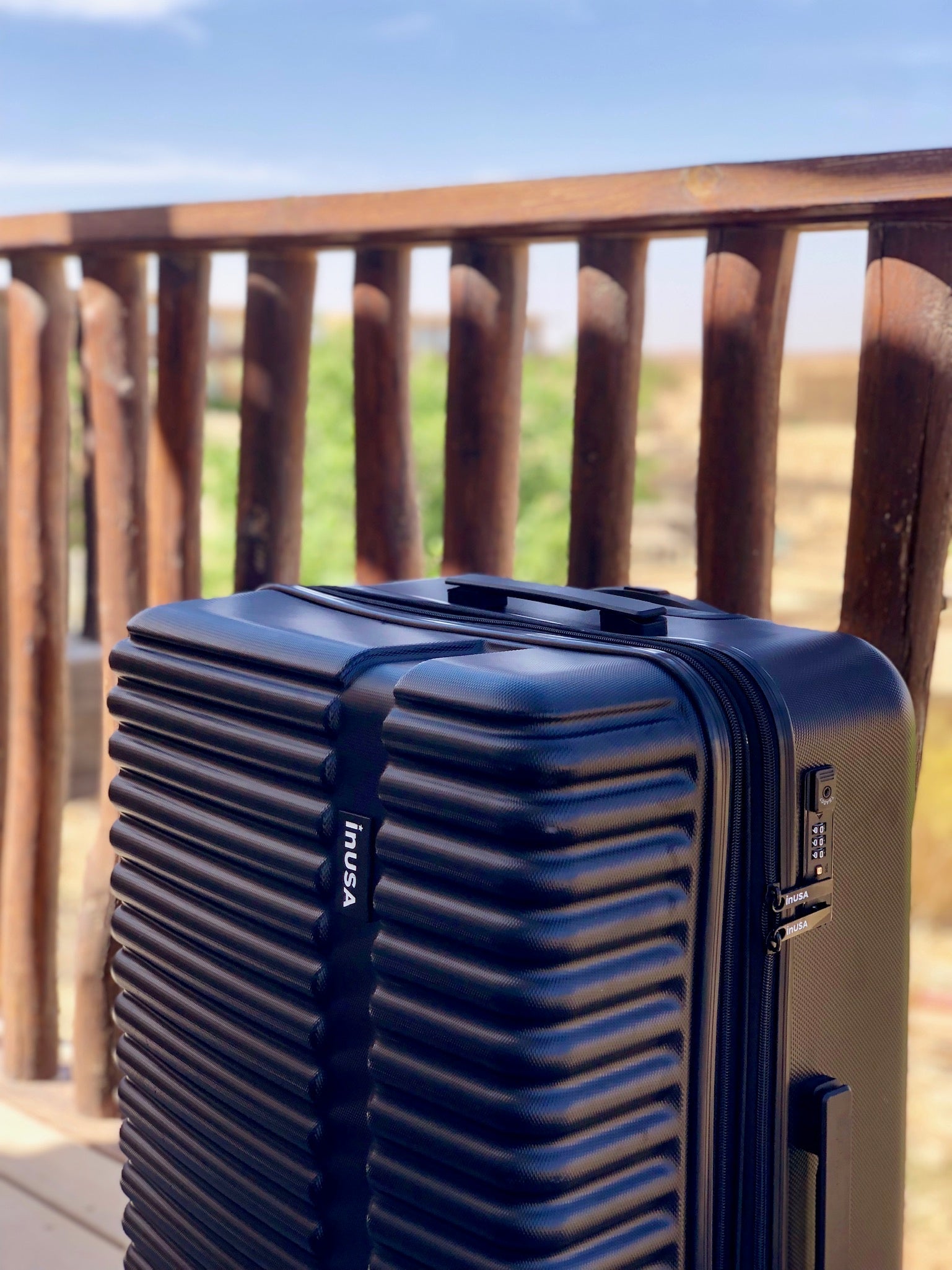 Black suitcase with a visible brand logo on a wooden deck with a scenic background.