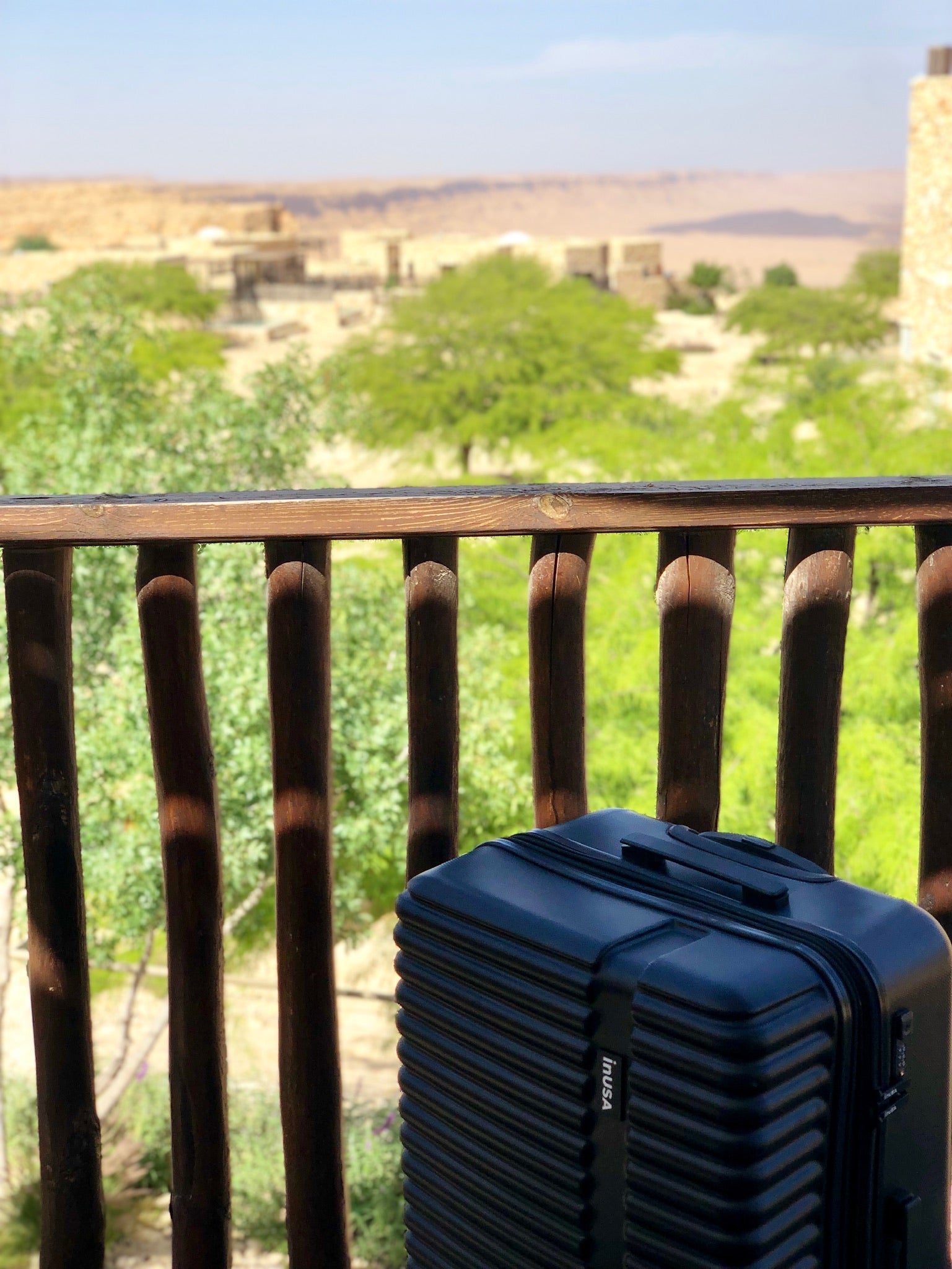 Blue suitcase on a balcony with a scenic view of trees and buildings in the background