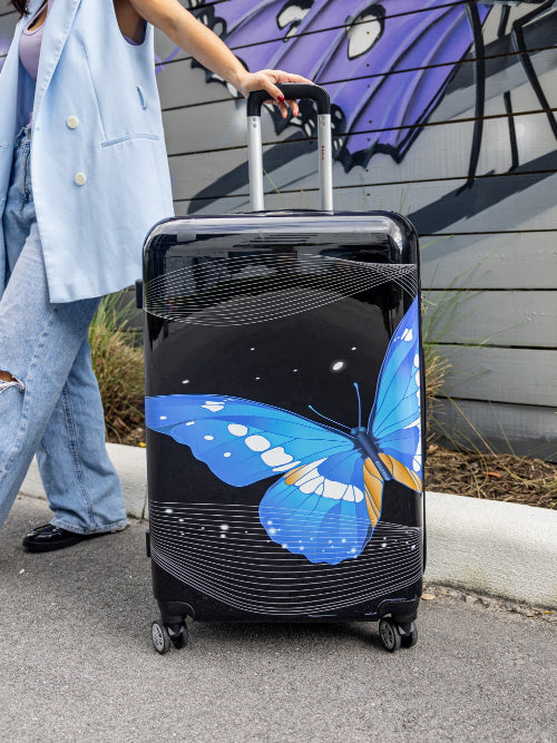 Person pulling a suitcase with a blue butterfly design against a mural background