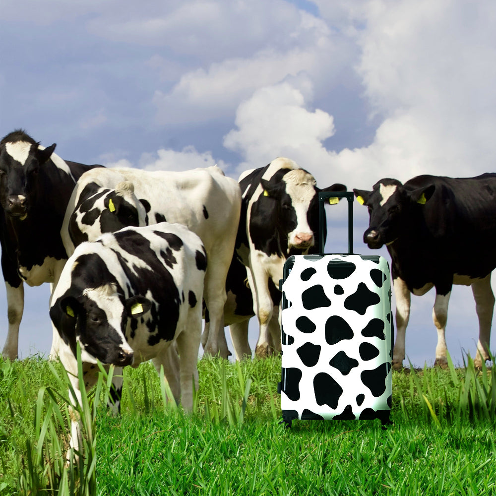 Cow-patterned suitcase in front of a group of cows in a field
