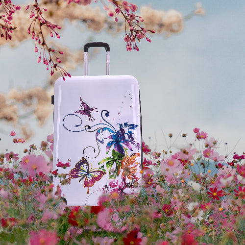 White suitcase with colorful butterfly design in a floral setting