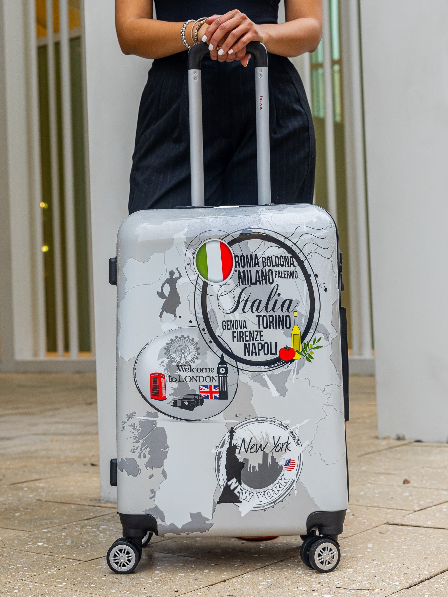 Person holding a gray suitcase with travel-themed stickers