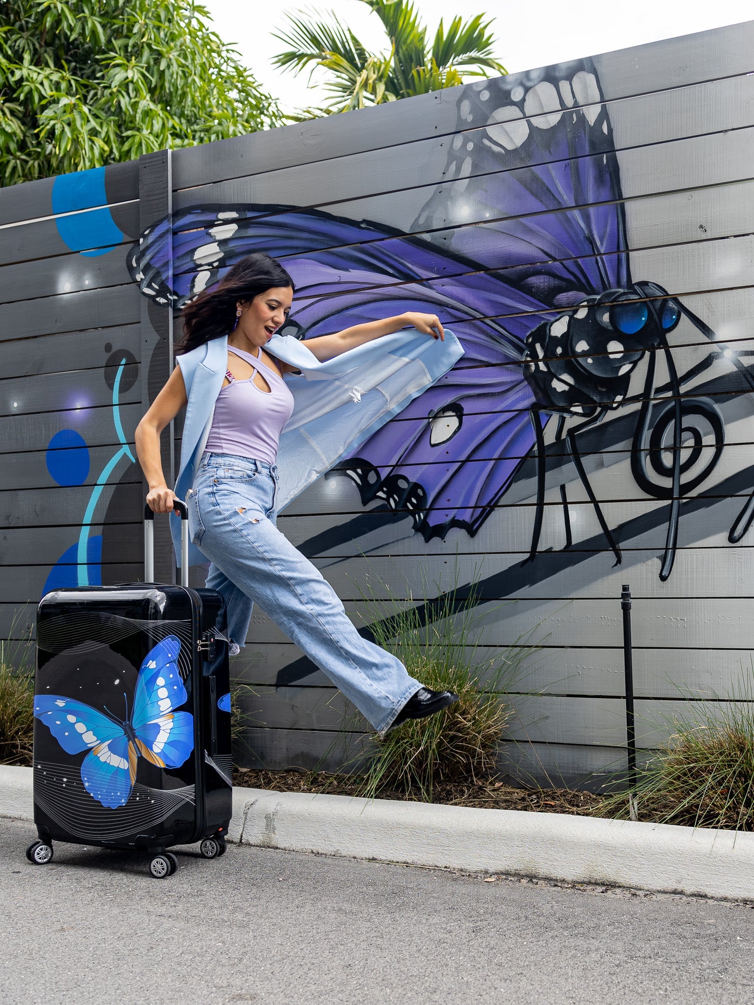 Woman with a suitcase featuring butterfly design in front of a wall with butterfly artwork