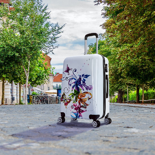 White suitcase with floral design on a street with trees and buildings in the background