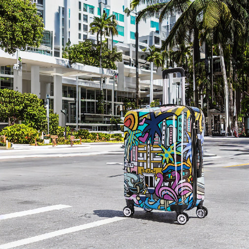 Colorful suitcase on a city street with palm trees and buildings in the background
