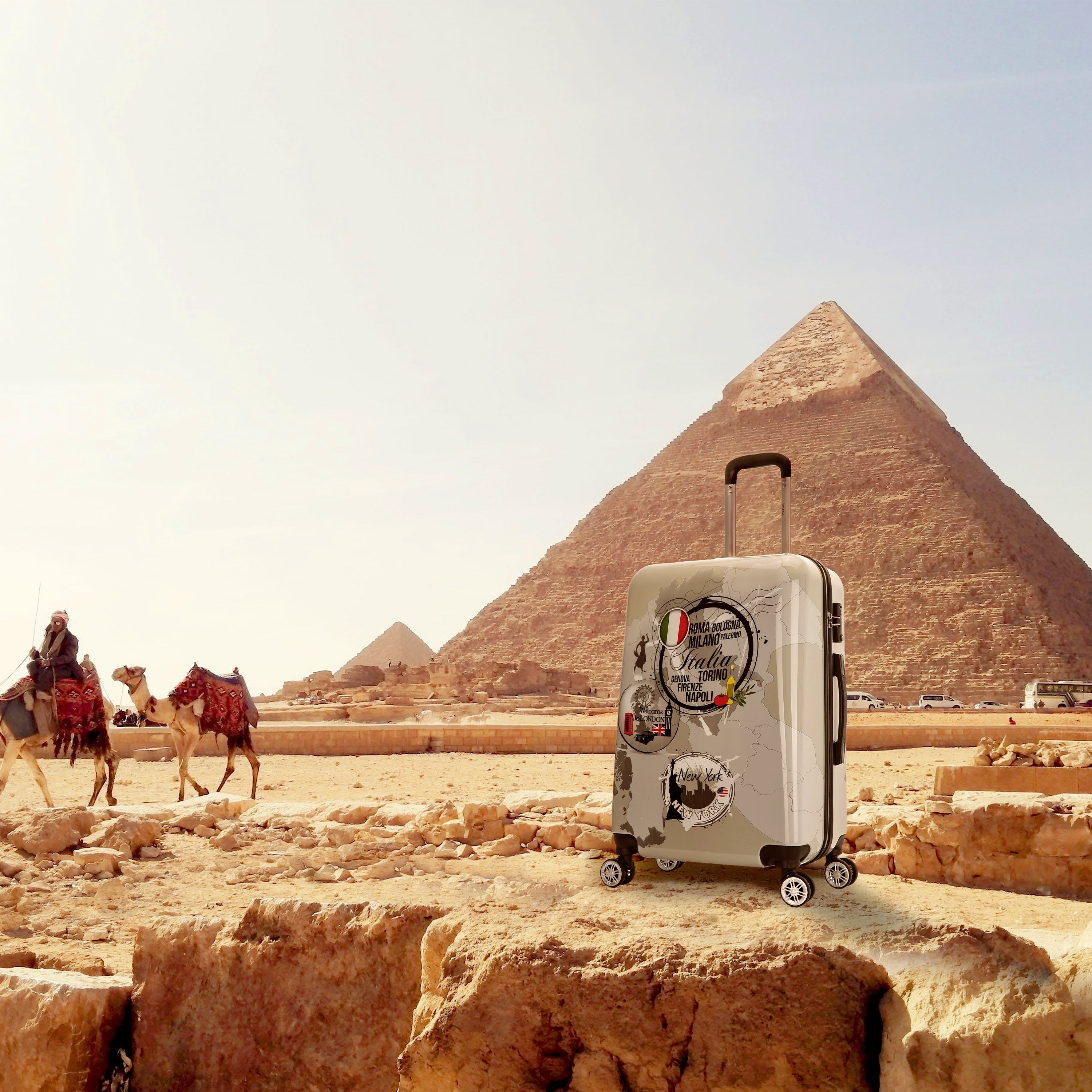 Suitcase with travel stickers in front of a pyramid and camels in the desert