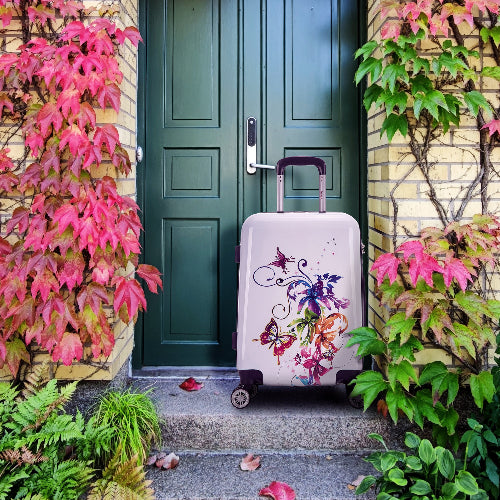 Floral-patterned suitcase in front of a green door with pink and green plants.