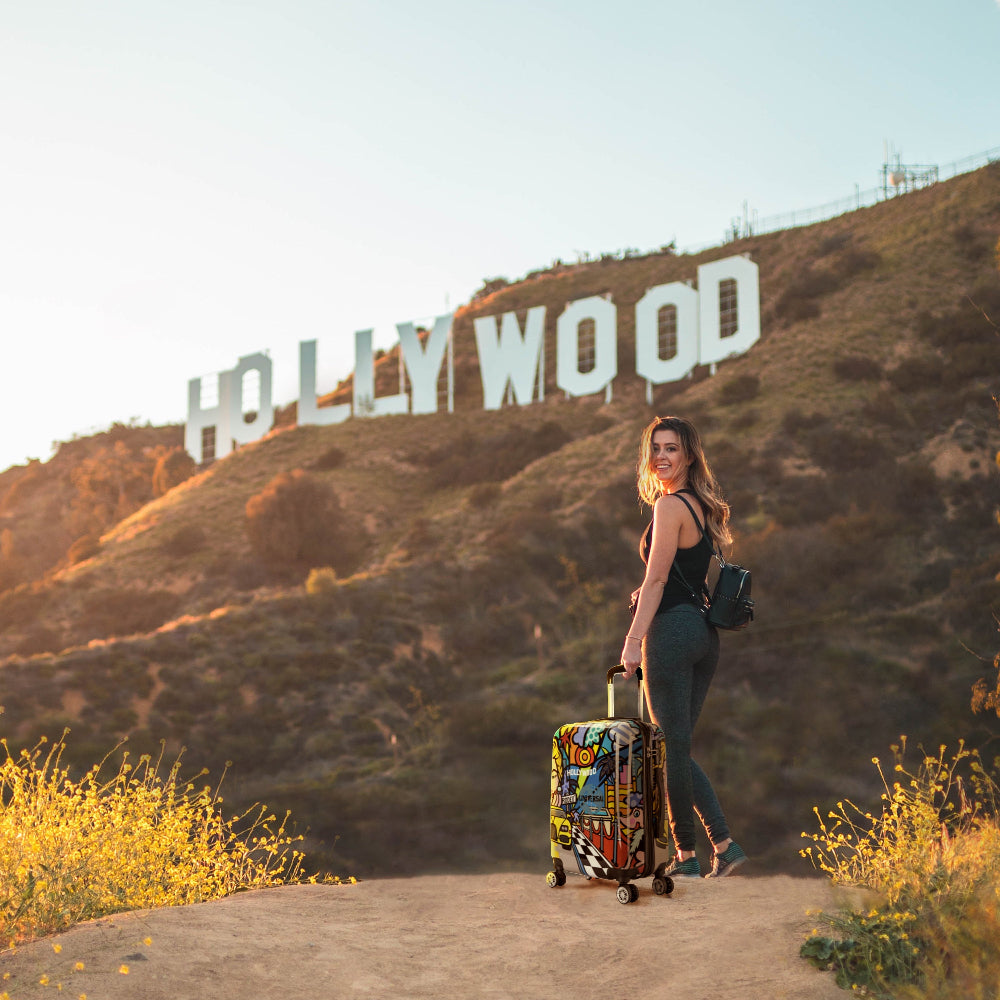 Woman with a colorful suitcase standing in front of the Hollywood sign.