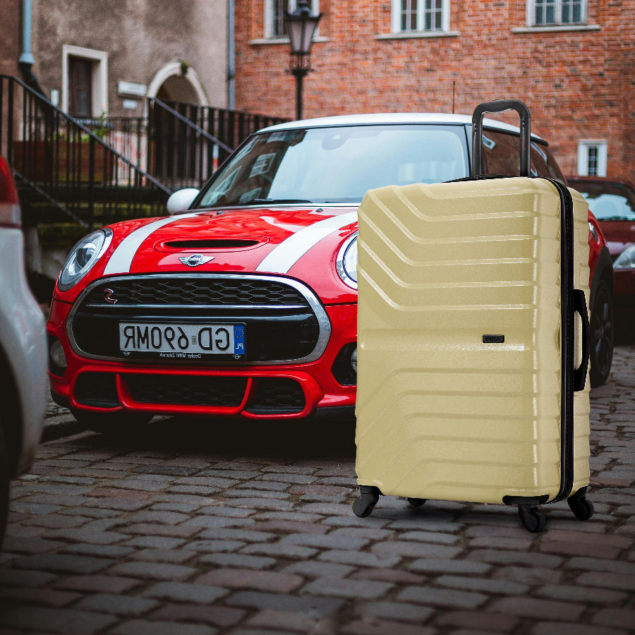 Beige suitcase in front of a red Mini Cooper car on a cobblestone street.