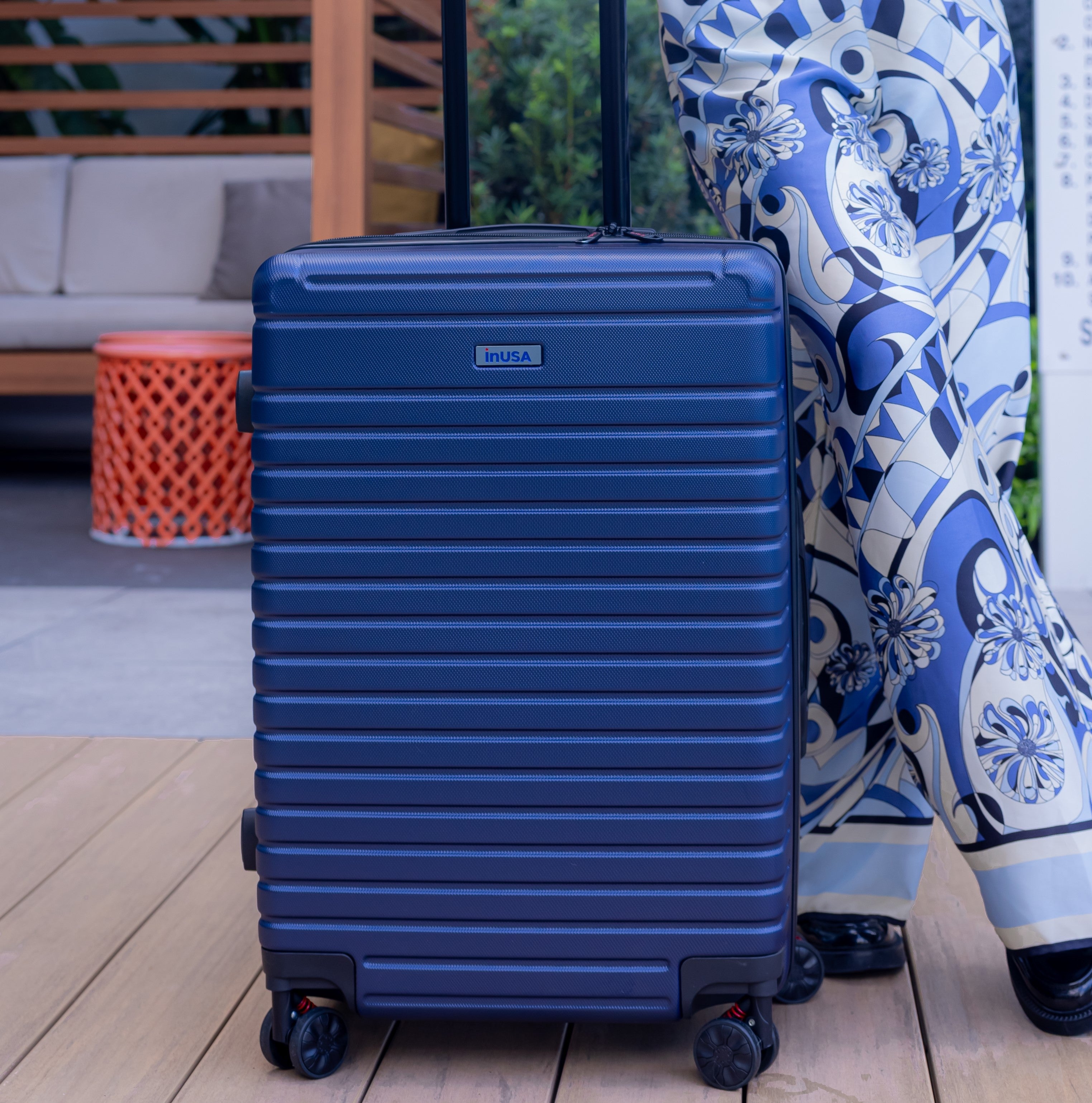 Blue suitcase on a wooden floor with a person wearing a blue and white patterned dress in the background.