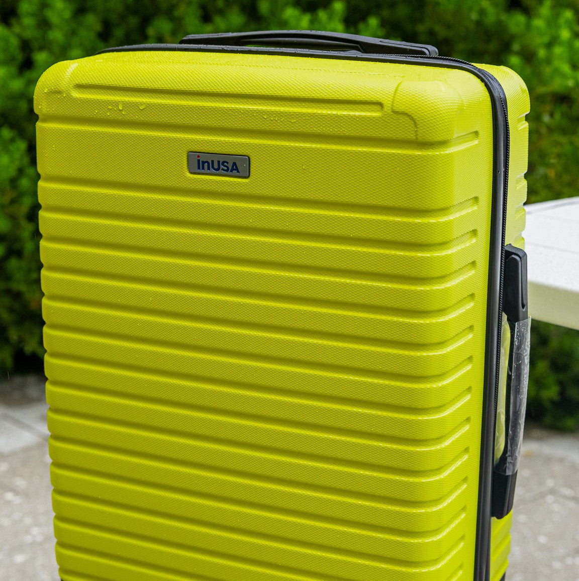 Yellow suitcase with 'inUSA' branding on a blurred outdoor background