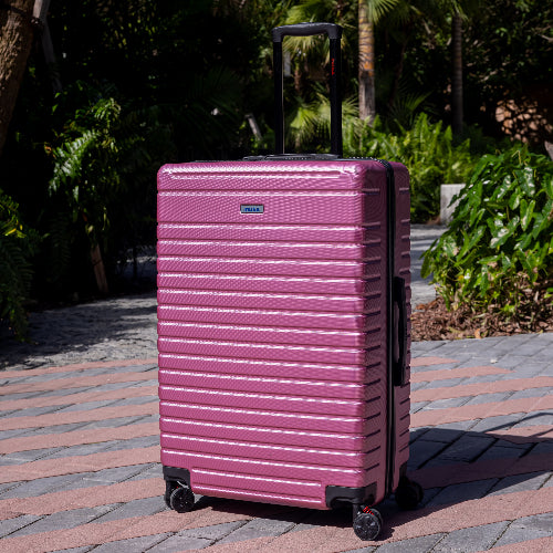Pink suitcase with a brand logo on a paved walkway with greenery in the background