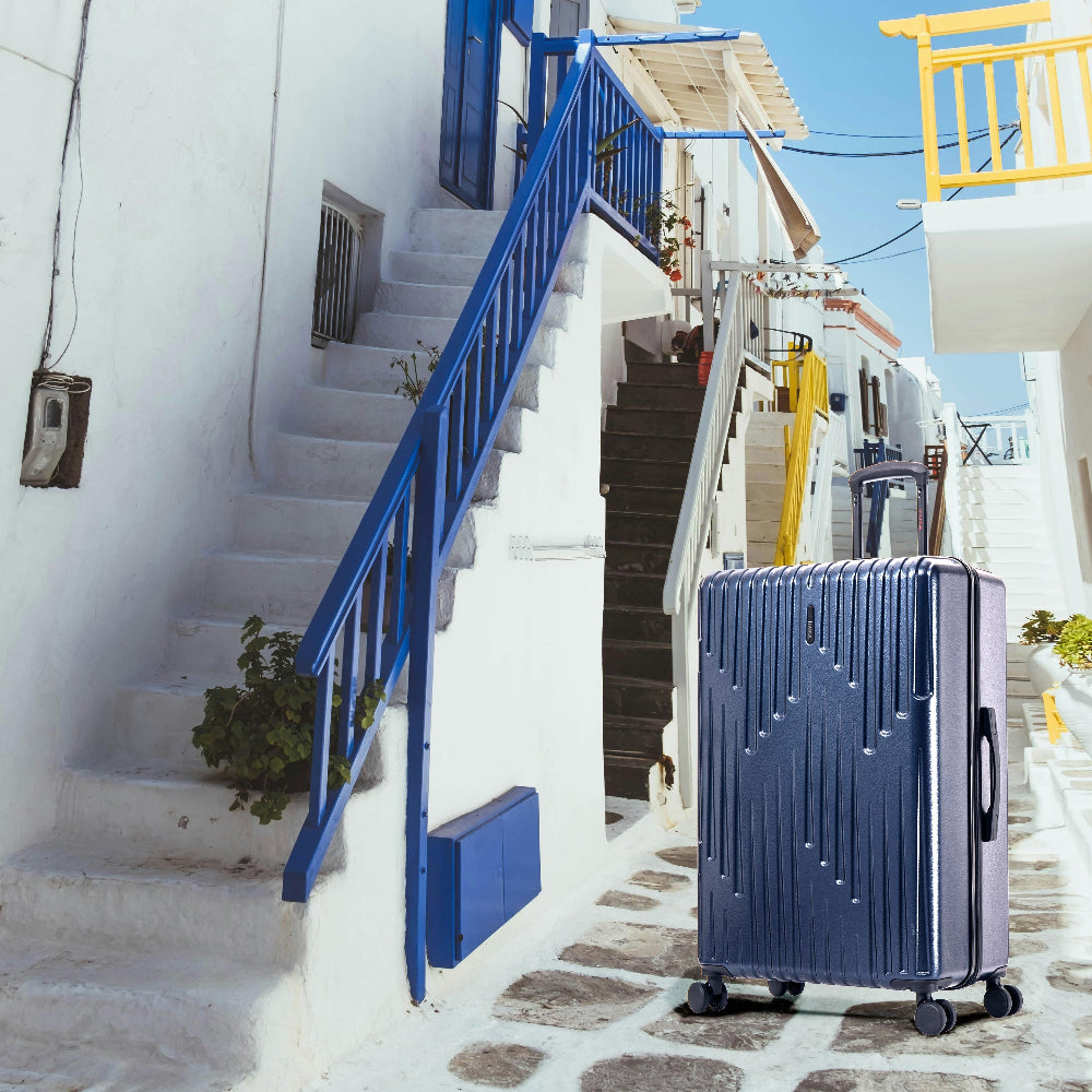 Blue suitcase on a cobbled street with white buildings and blue railings.