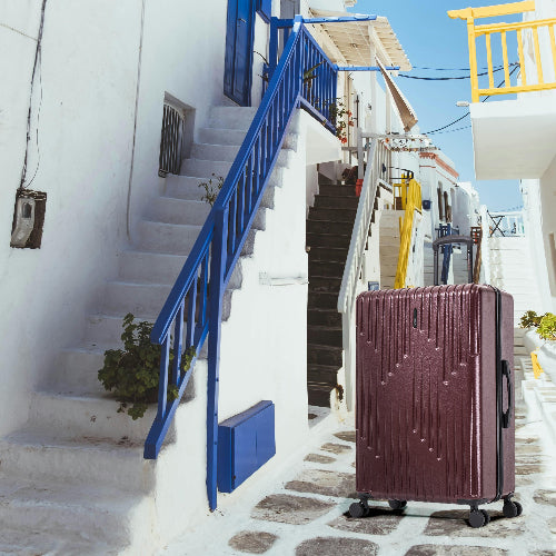 Brown suitcase on a cobbled street with white buildings and blue railings in the background