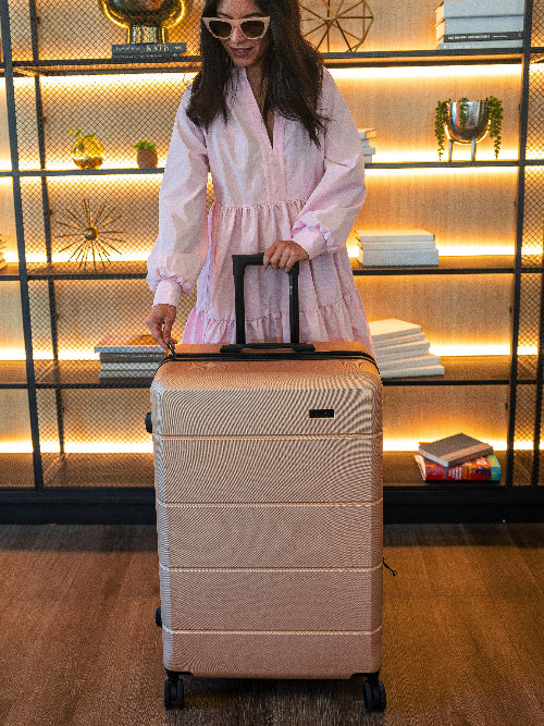 Woman in a pink robe holding a beige suitcase in a room with shelves and books.
