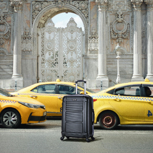 Black suitcase in front of yellow taxis with an ornate building in the background